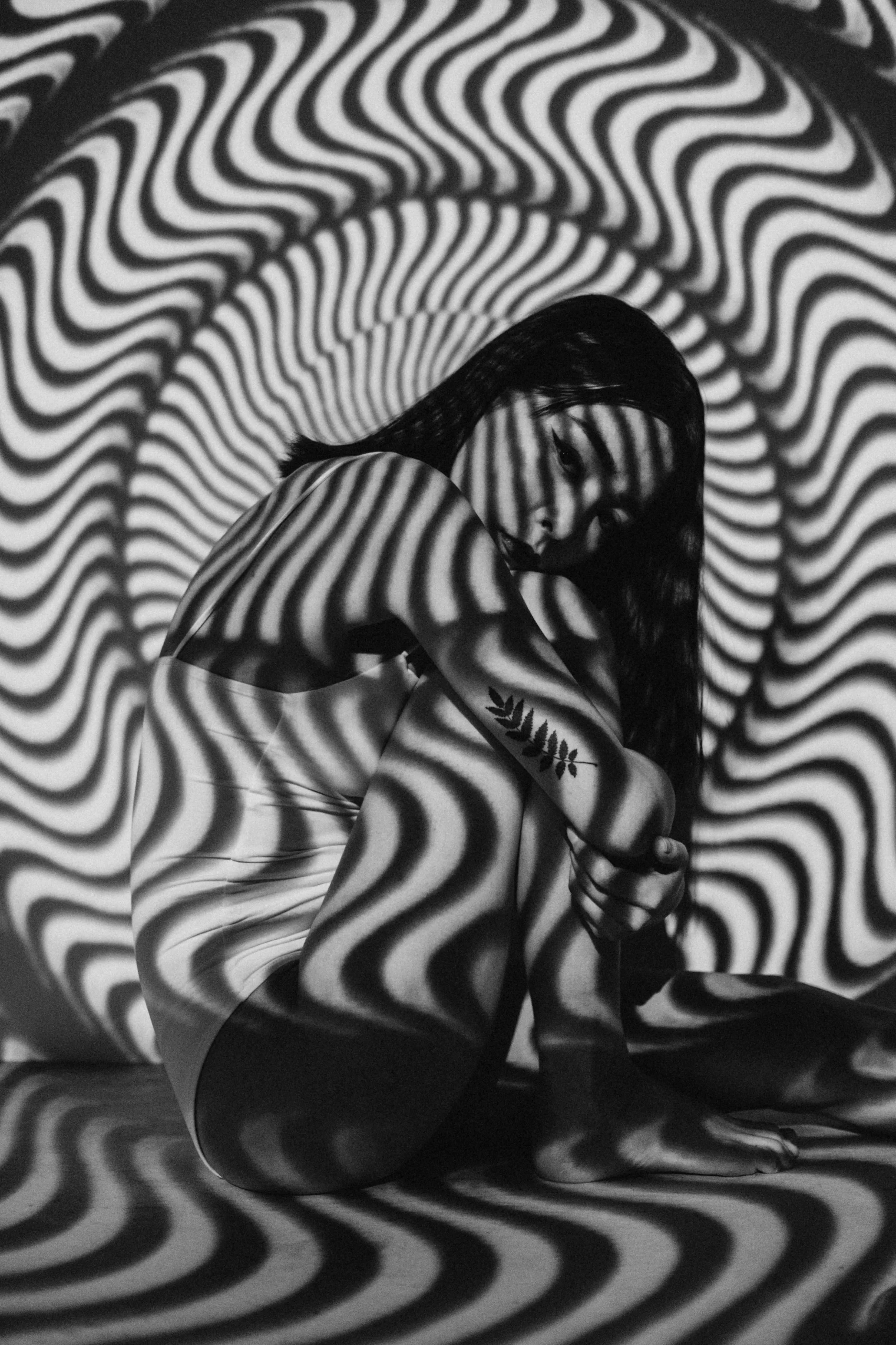 A person sitting with a projected black and white wavy pattern on their body and background.