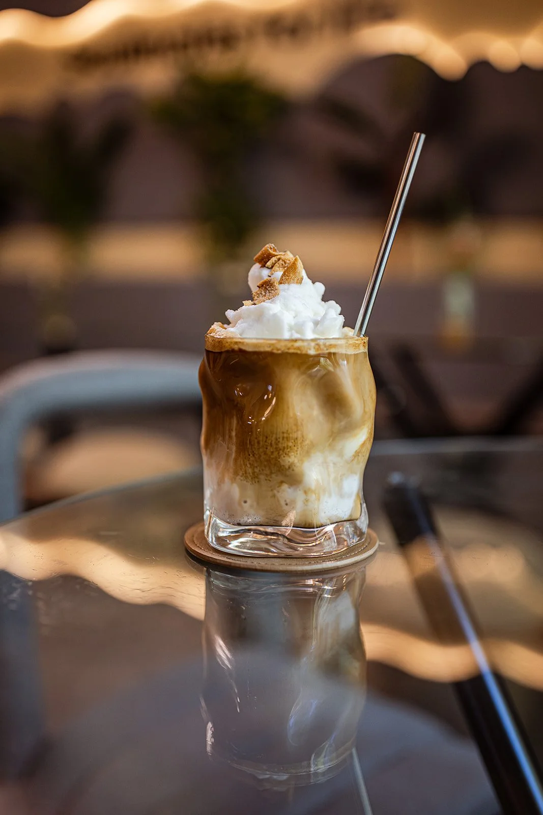 Ein Glas mit Kaffee, Milch und Eis, garniert mit Schlagsahne und Keksen, auf einem Tisch im Café.
