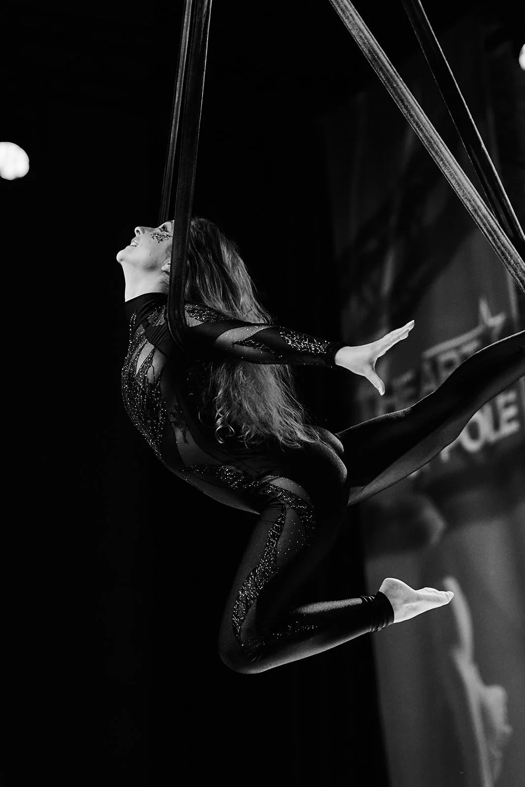 Schaukelnde Artistin in einem schwarzen, glitzernden Kostüm bei einer Pole-Vorstellung