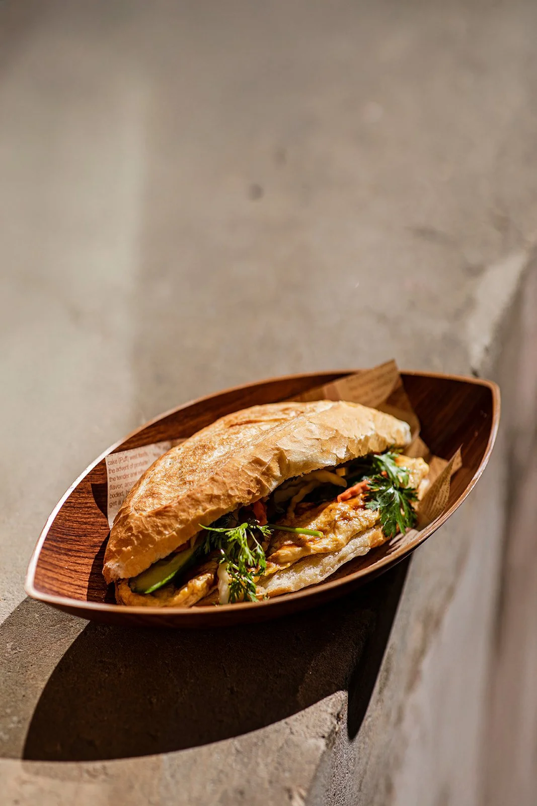 Sandwich mit Fleisch, Gurken, Tomaten und Kräutern in einem Holzschale auf einem Steinmauernboden.