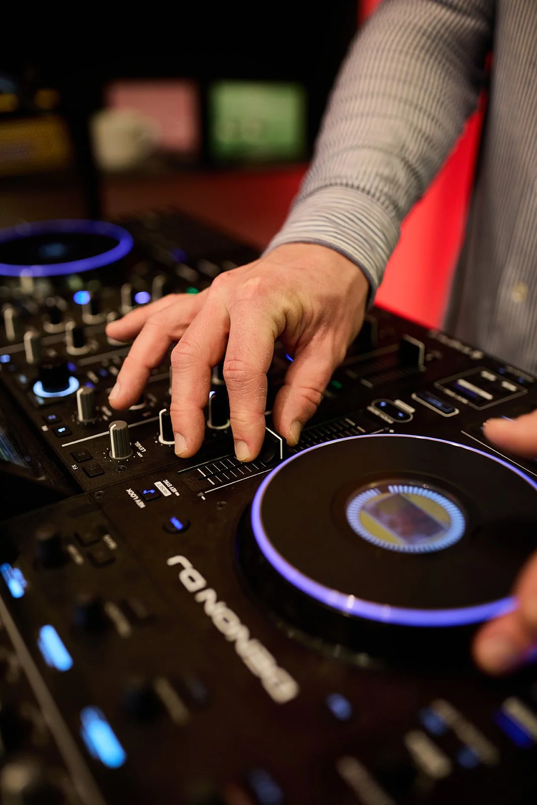 Eine Person bedient ein DJ-Controller mit leuchtenden Knöpfen und Drehreglern.
