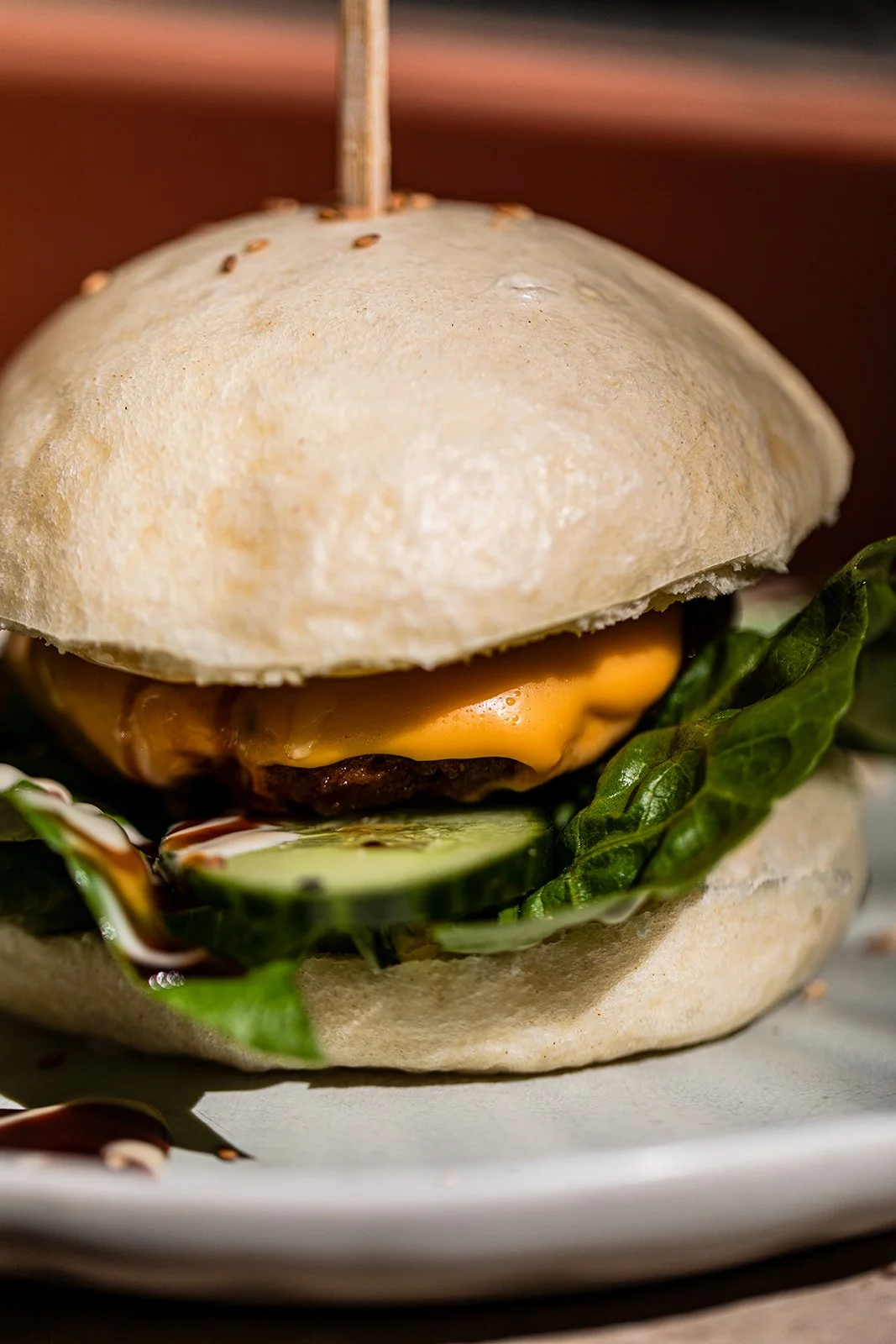 Ein Burger mit Brötchen, Salat, Gurken, Käse, und einer Hackfleischpatty, serviert auf einem Teller.