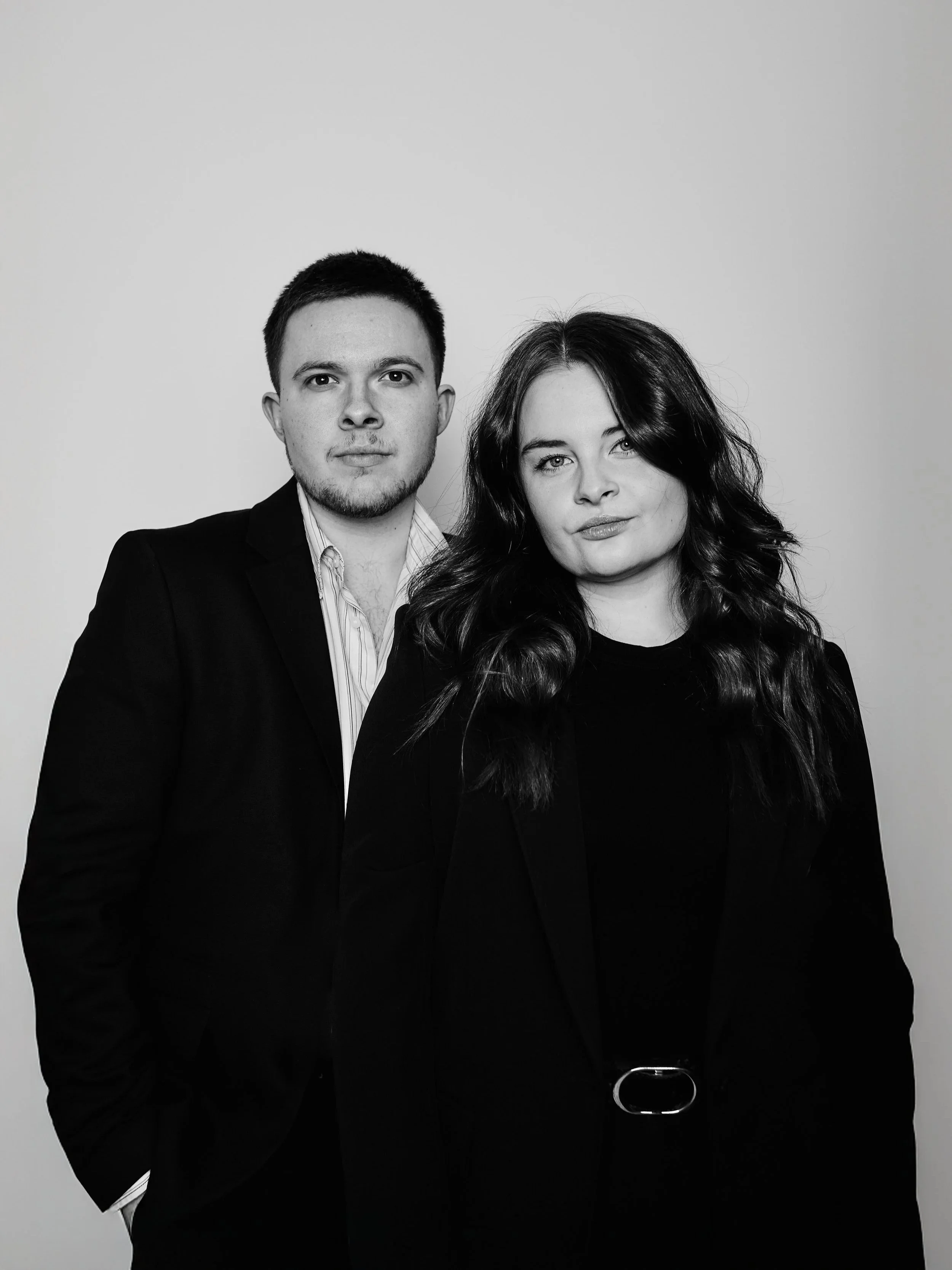 Ein Schwarzw-white-Foto eines Mannes und einer Frau, beide in dunklen Anzügen, vor einem hellen Hintergrund.