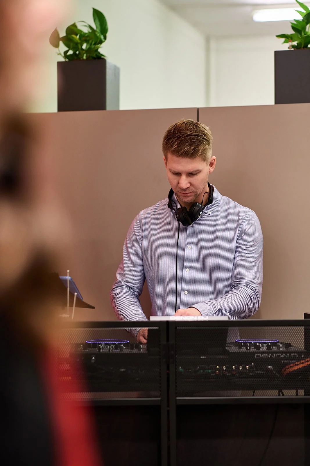 Ein junger Mann mit Kopfhörern am Hals, der an einem DJ-Deck arbeitet.