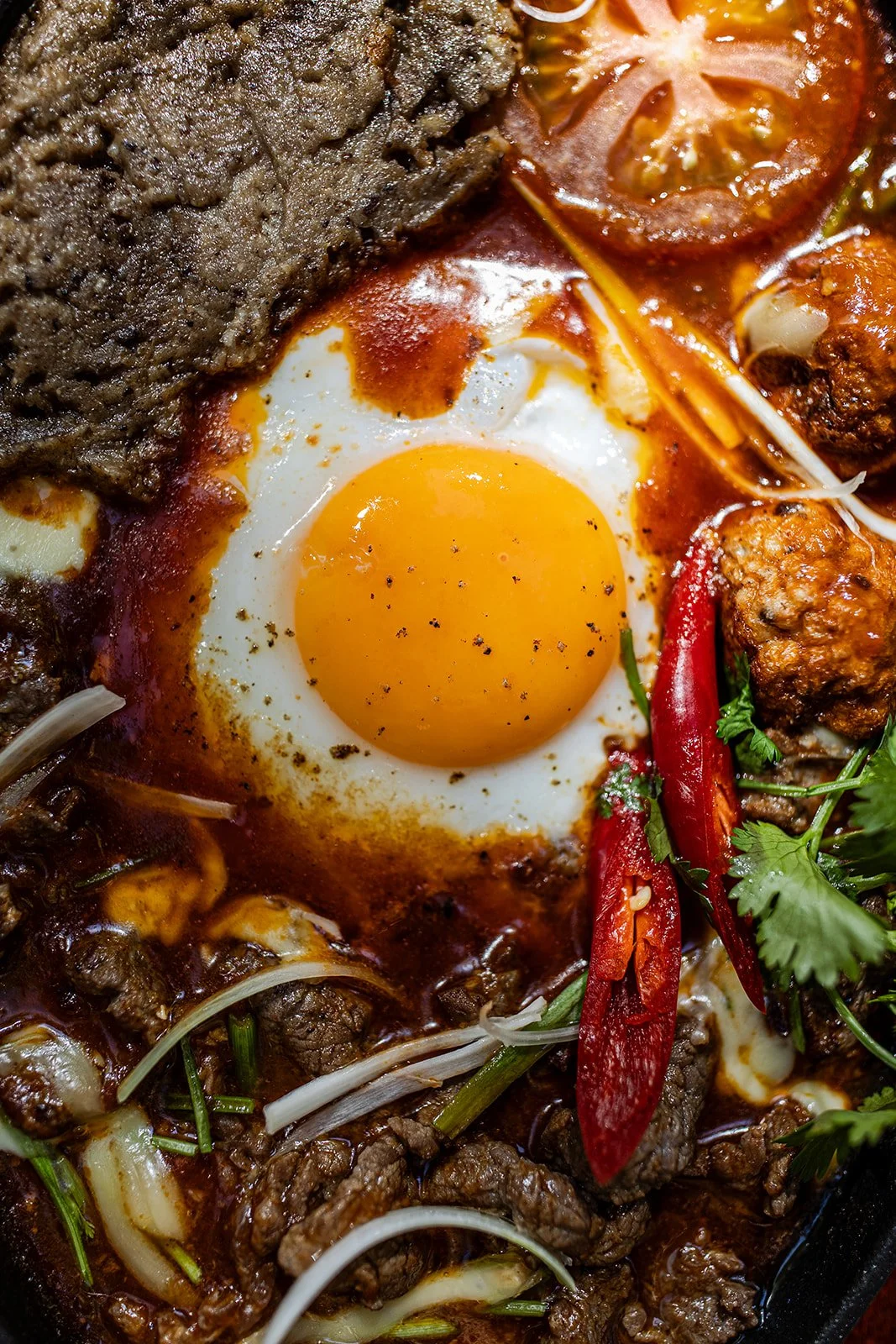 Ein Teller mit einem Spiegelei, Rindfleisch, Tomaten, Chili, Koriander, Zwiebeln und Gewürzen.