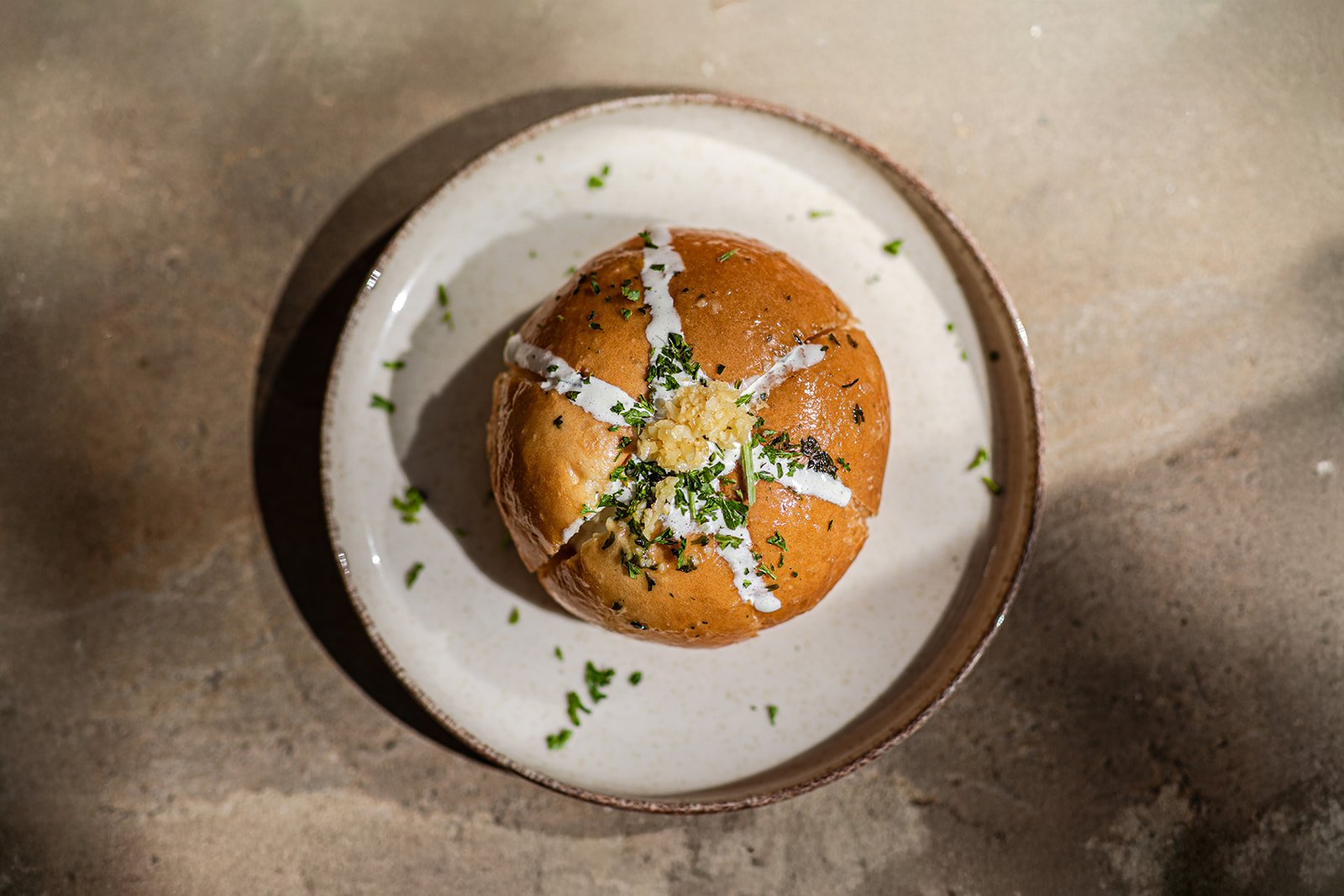 Eine Schüssel mit einer aufgeschnittenen gekochten Kartoffel, garniert mit Knoblauch, Petersilie und einer weißen Sauce.