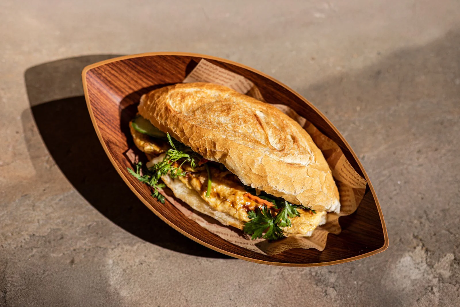 Ein Sandwich mit Hähnchen, Gemüse und Kräutern in einem Holzschale auf einem Tisch.
