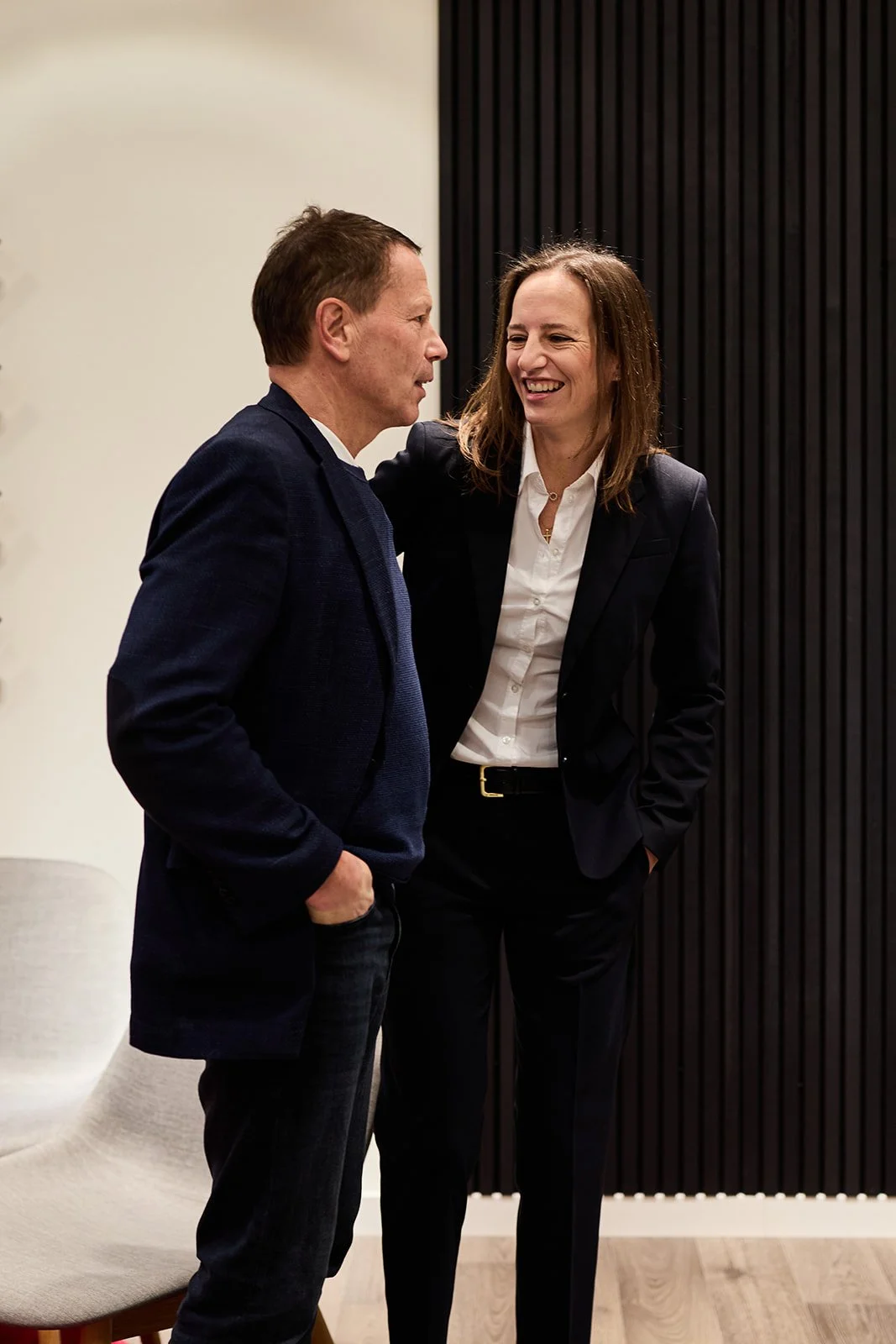 Ein Mann und eine Frau im Gespräch, die lächelnd miteinander sprechen, in einem modernen Innenraum.