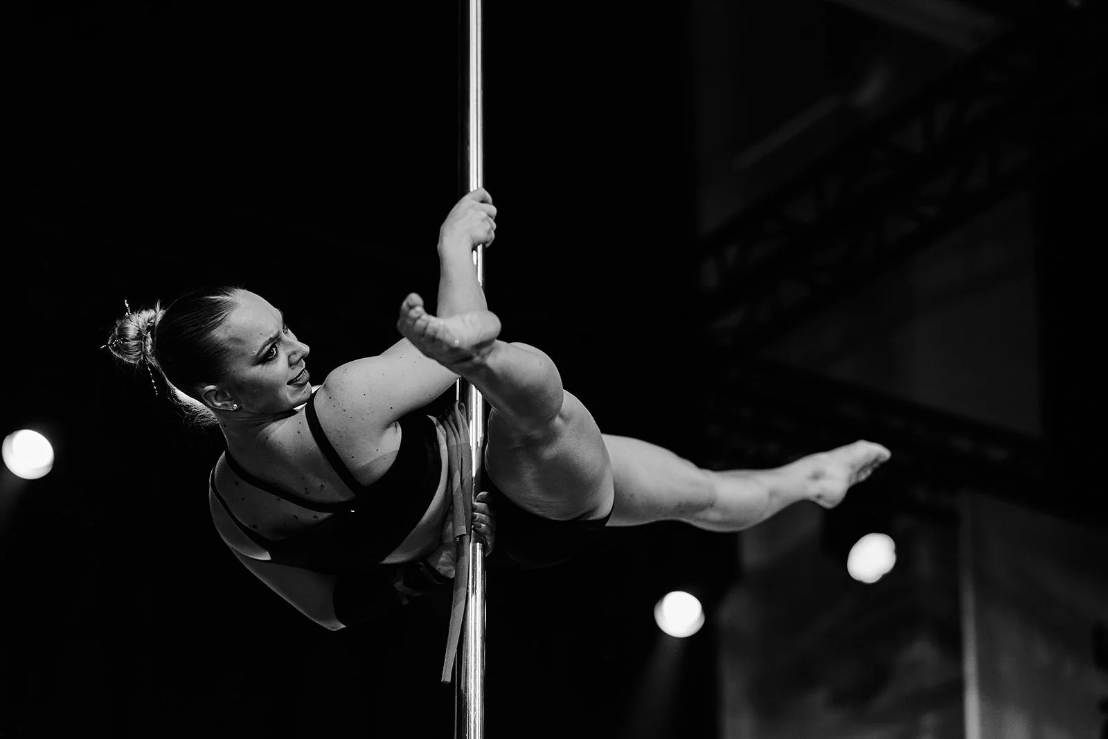 Eine Turner auf einem vertikalen Stab bei einer Pole Dance Aufführung, schwarz-weiß, im dunklen Raum.