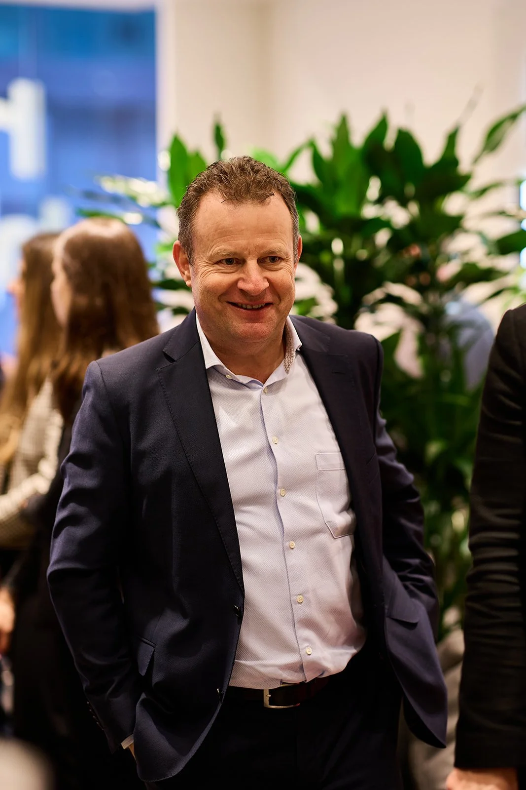 Mann in dunklem Anzug und weißem Hemd lächelnd bei einer Veranstaltung.