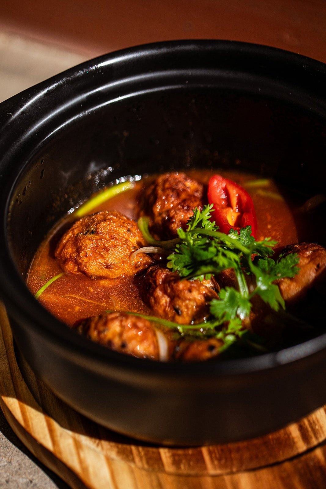 Schüssel mit Fleischbällchen in Tomatensoße, garniert mit frischer Koriander und roten Paprikastreifen.