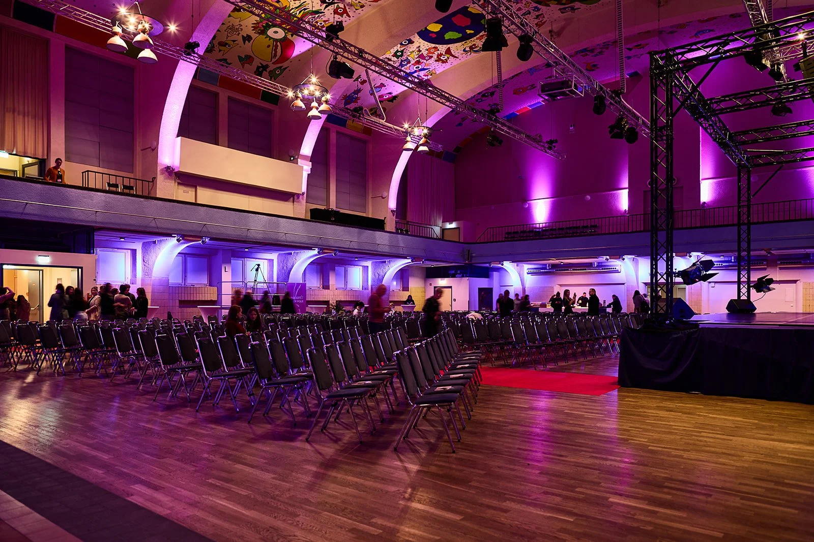 Leeres Veranstaltungsraum mit Stuhlreihen, Bühne, buntem Deckenmuster und bunte Beleuchtung für eine Veranstaltung.