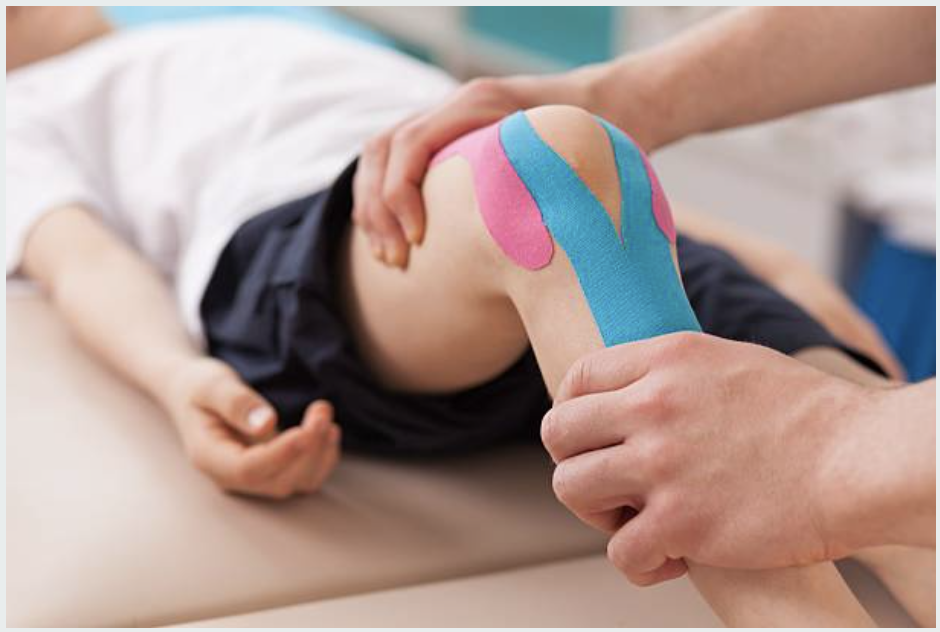 Child receiving knee therapy with colored elastic tape applied on the knee.