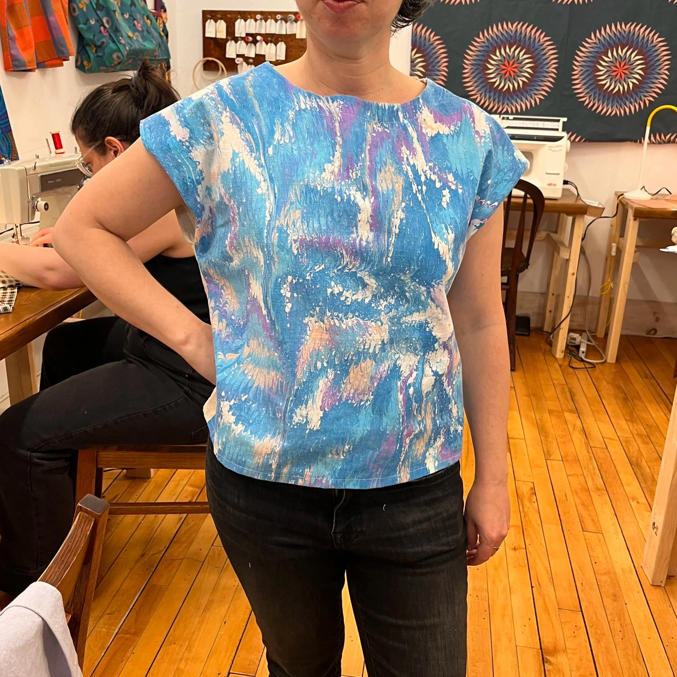 A woman wearing a blue, purple, and white tie-dye patterned top made in the skills sewing class where you can make, mend, or alter sewing projects.