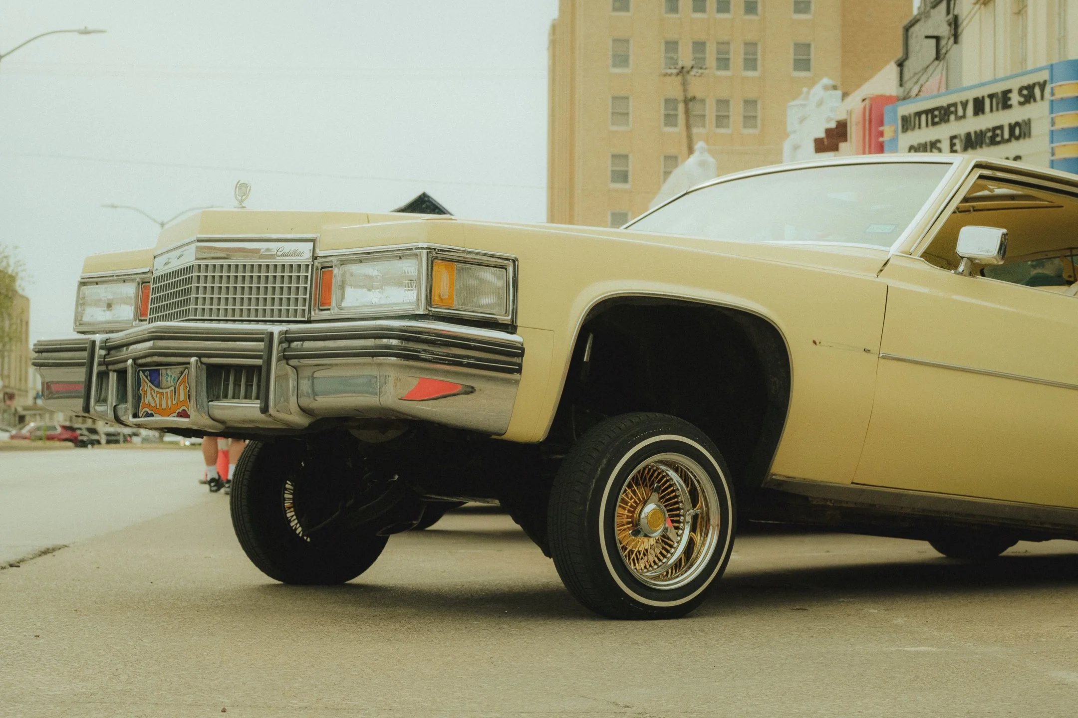 A vintage yellow Cadillac car with one wheel lifted off the ground parked on the street Photographed in Dallas Texas