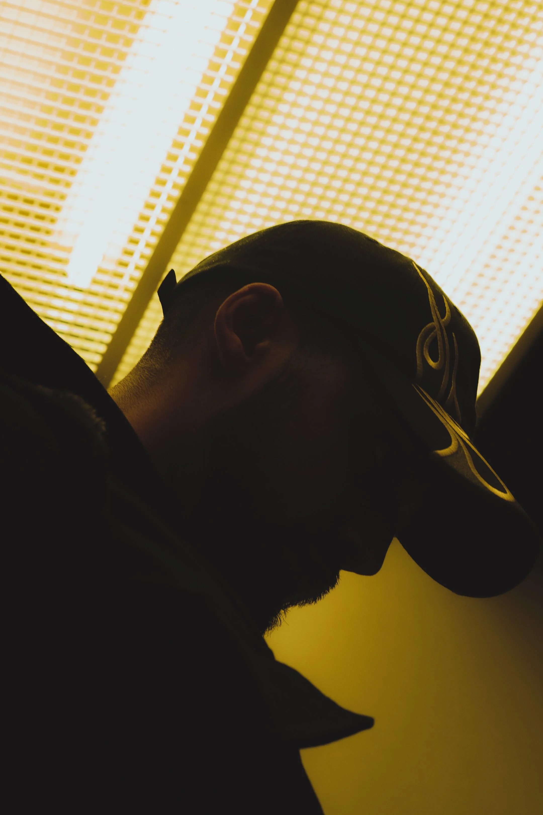 Silhouette of a person wearing a cap, backlit by a yellowish light coming from above.