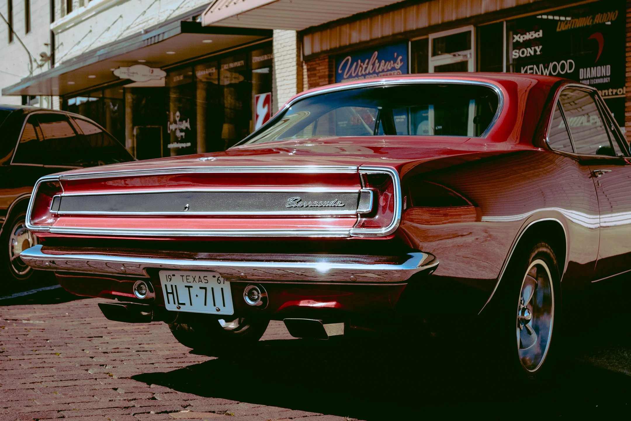Red vintage Buick Riviera car parked on brick street outside storefronts in Dallas Texas