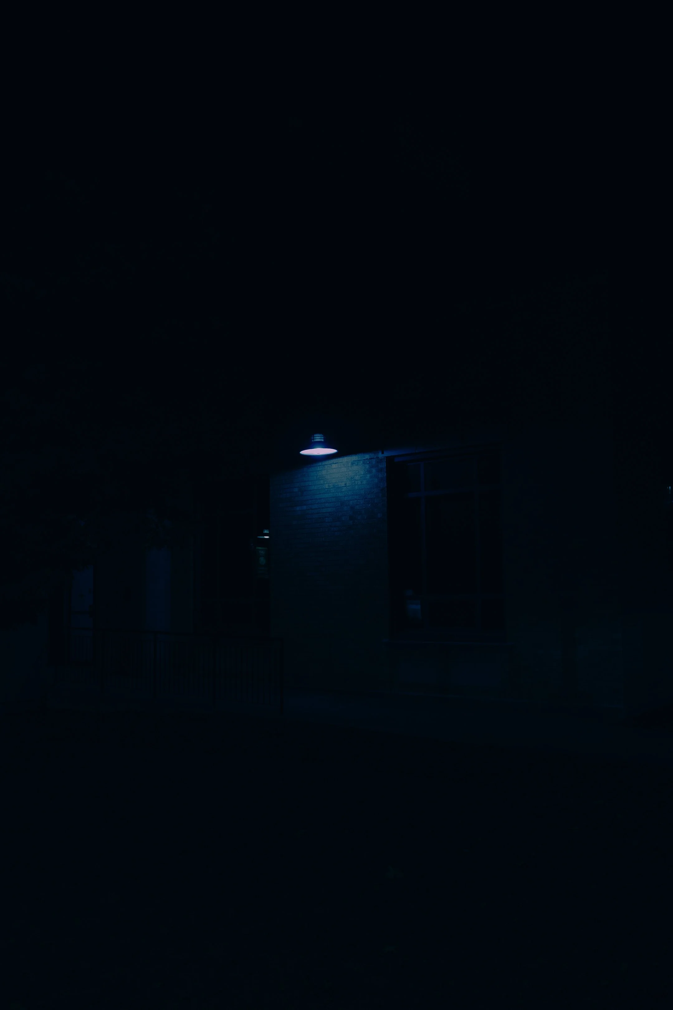 A dark outdoor scene with a building illuminated by a blue-toned exterior light.