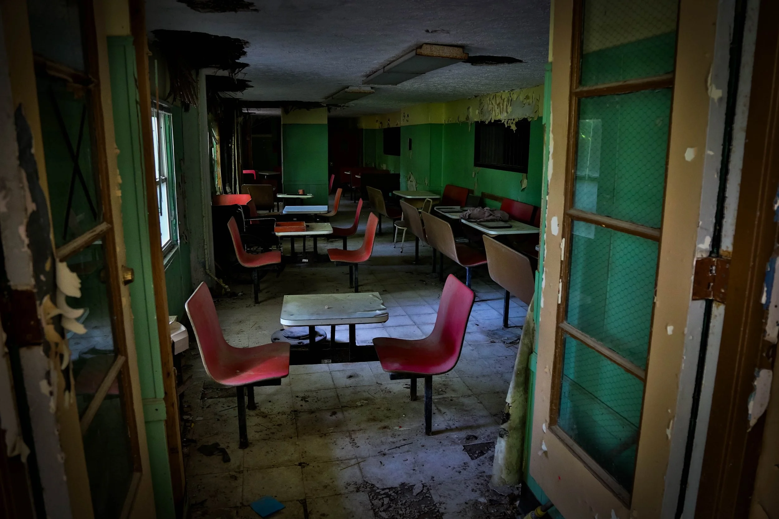 A dark, deteriorated corridor with peeling paint and a damaged security gate or door.