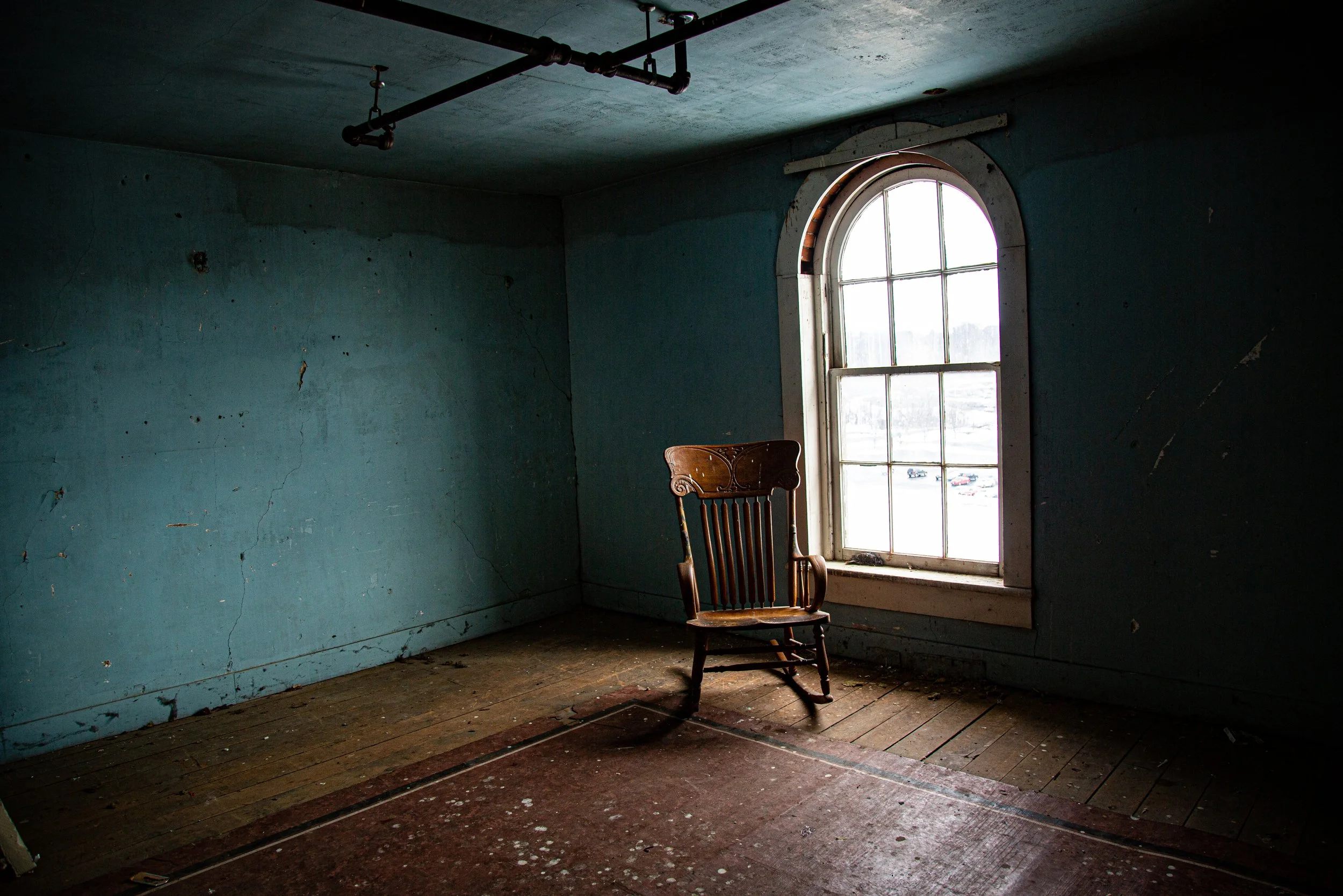 An abandoned, rusted door with peeling paint in a dimly lit, dilapidated building hallway.
