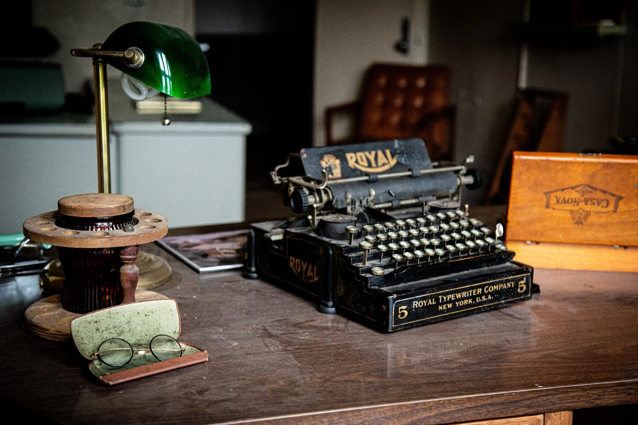 An open book on a rusty desk in a dimly lit room, with a chalkboard and a closed door in the background.
