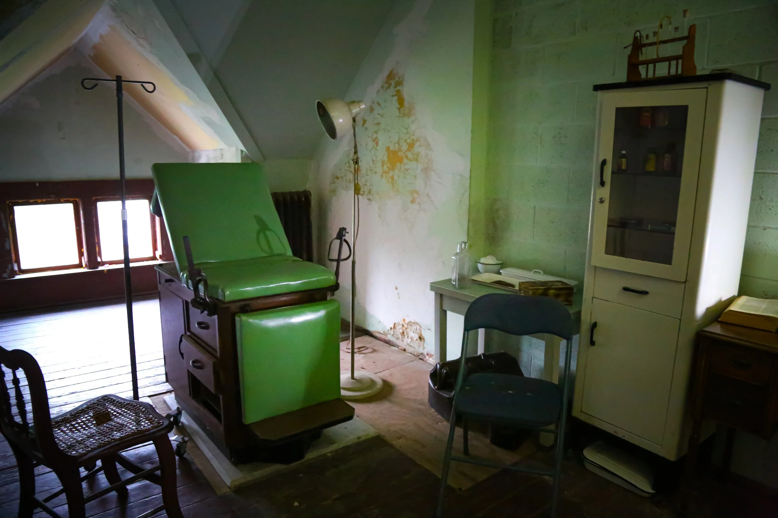 Dark interior hallway with a chain hanging from the wall, leading to a staircase and doorway in a partially lit room.