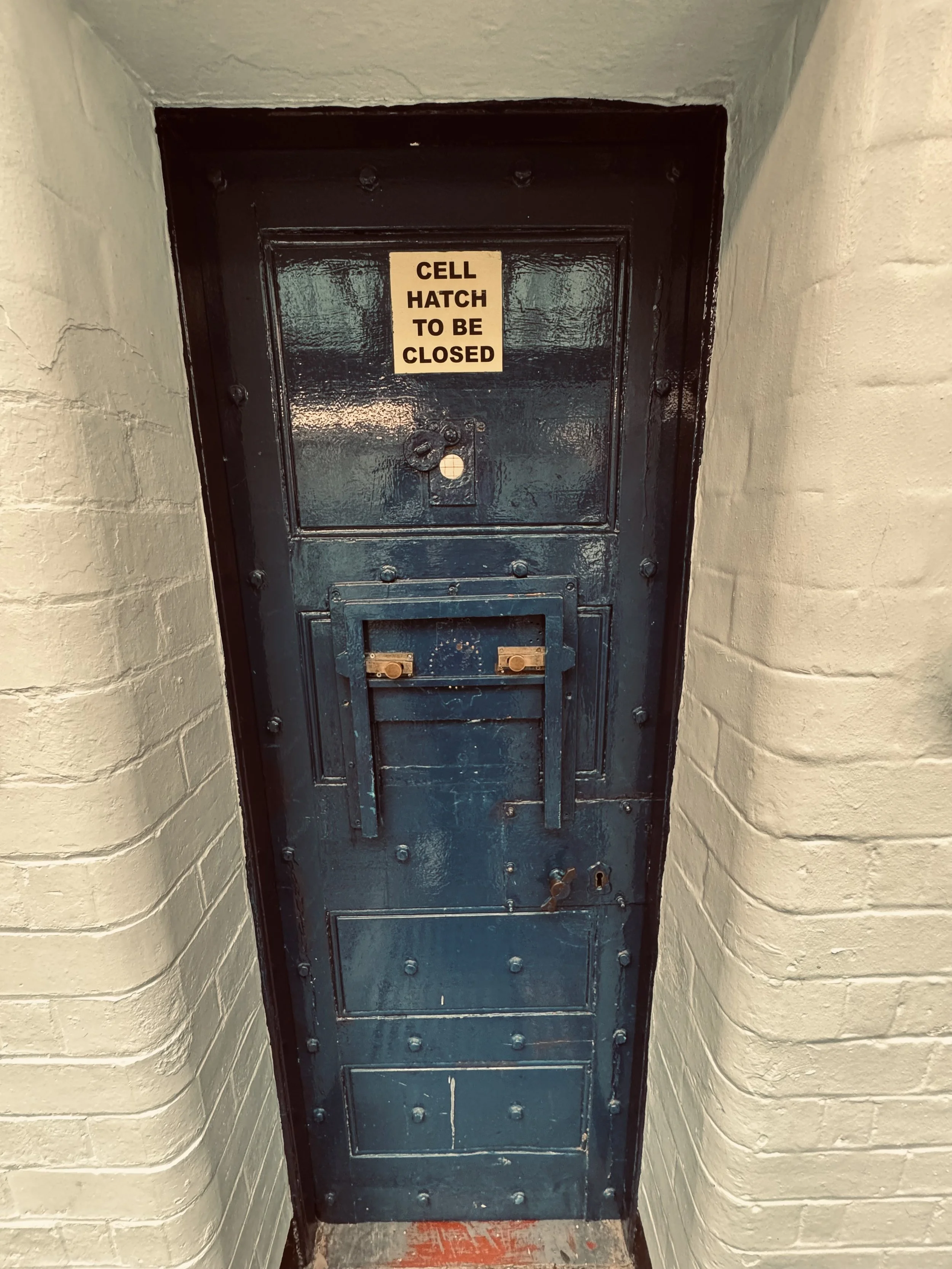 A dark green metal door with a sign that reads 'Cell Hatch to be Closed' in black text on a yellow background.