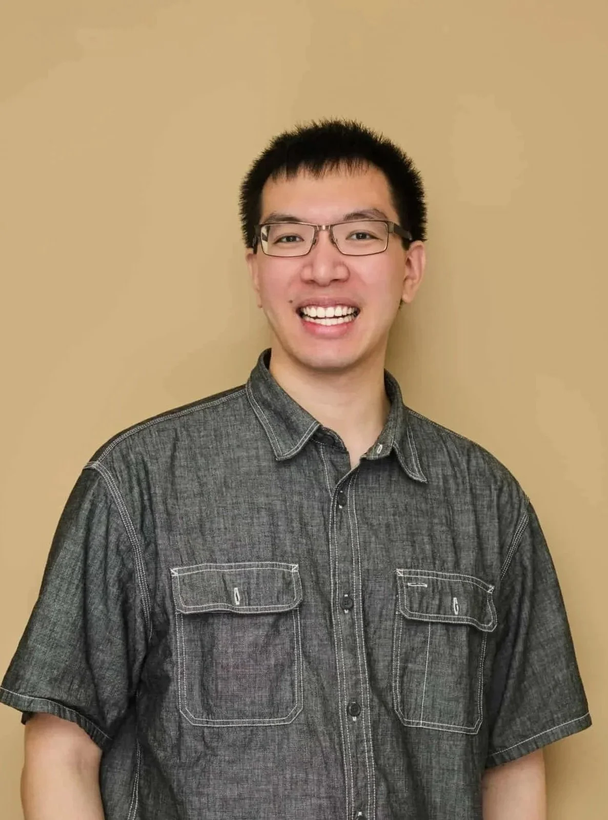 Man wearing glasses and a suit with a blue tie smiling against a plain background.