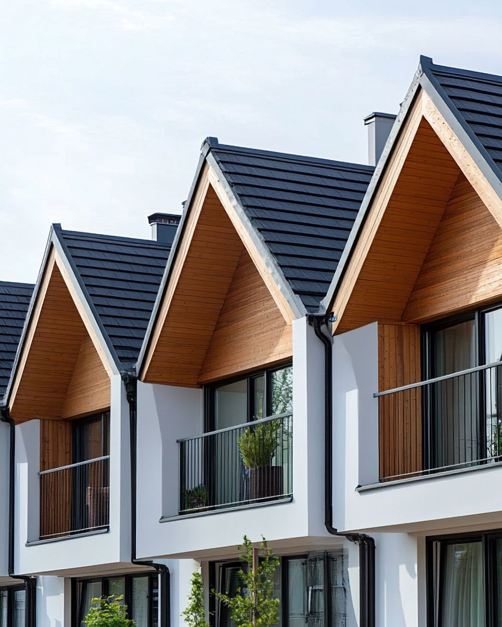 Modern residential building with black-tiled gabled roofs, white exterior walls, wooden accents, and glass balconies.