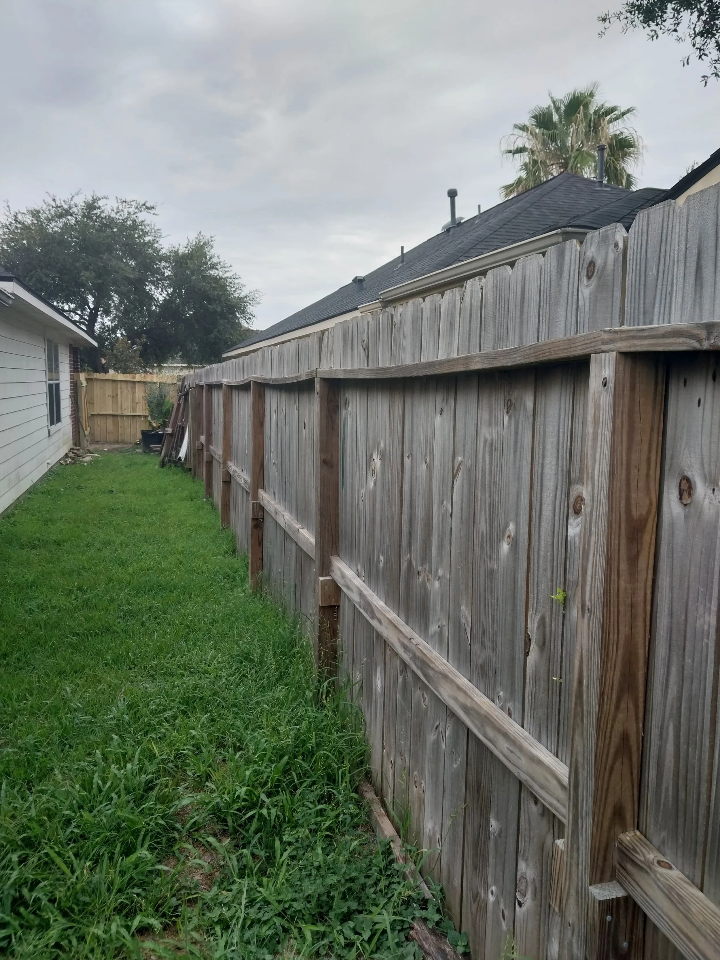 Wooden fence along a grassy yard with a house on the left and a cloudy sky above.