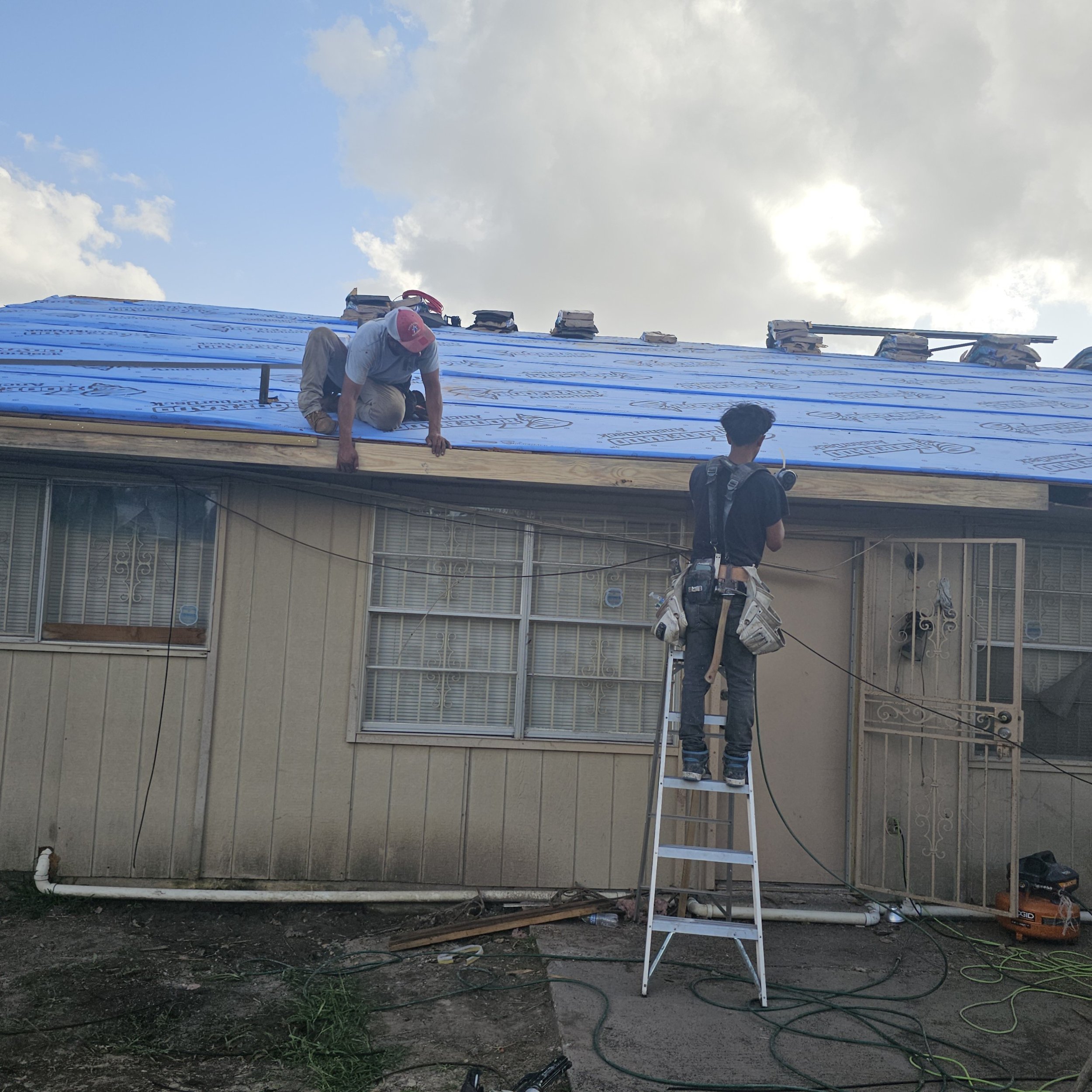 Construction workers installing siding on a house, with one worker on scaffolding and materials and tools around them.