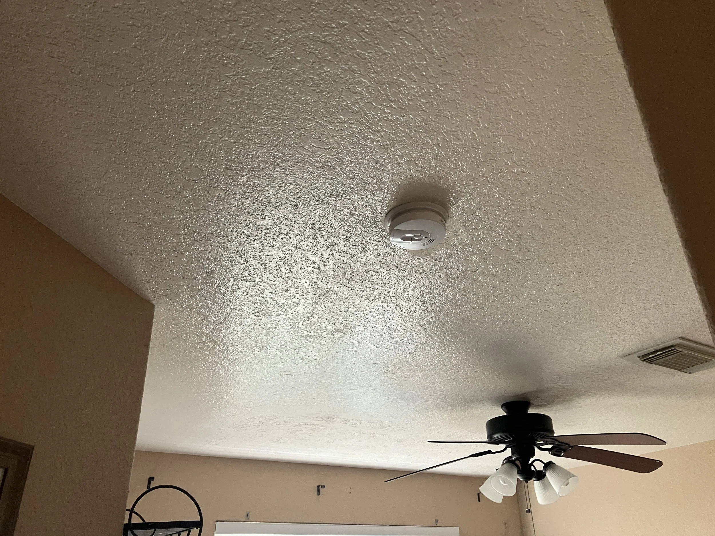 Ceiling fan with light fixtures on beige textured ceiling, corner of room visible.