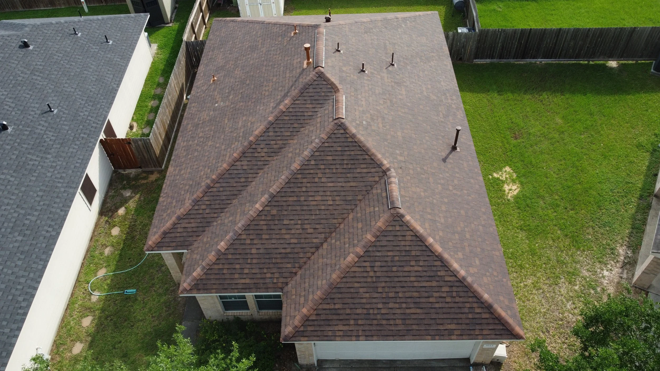 An aerial view of a house with a brown roof and a backyard surrounded by fences.