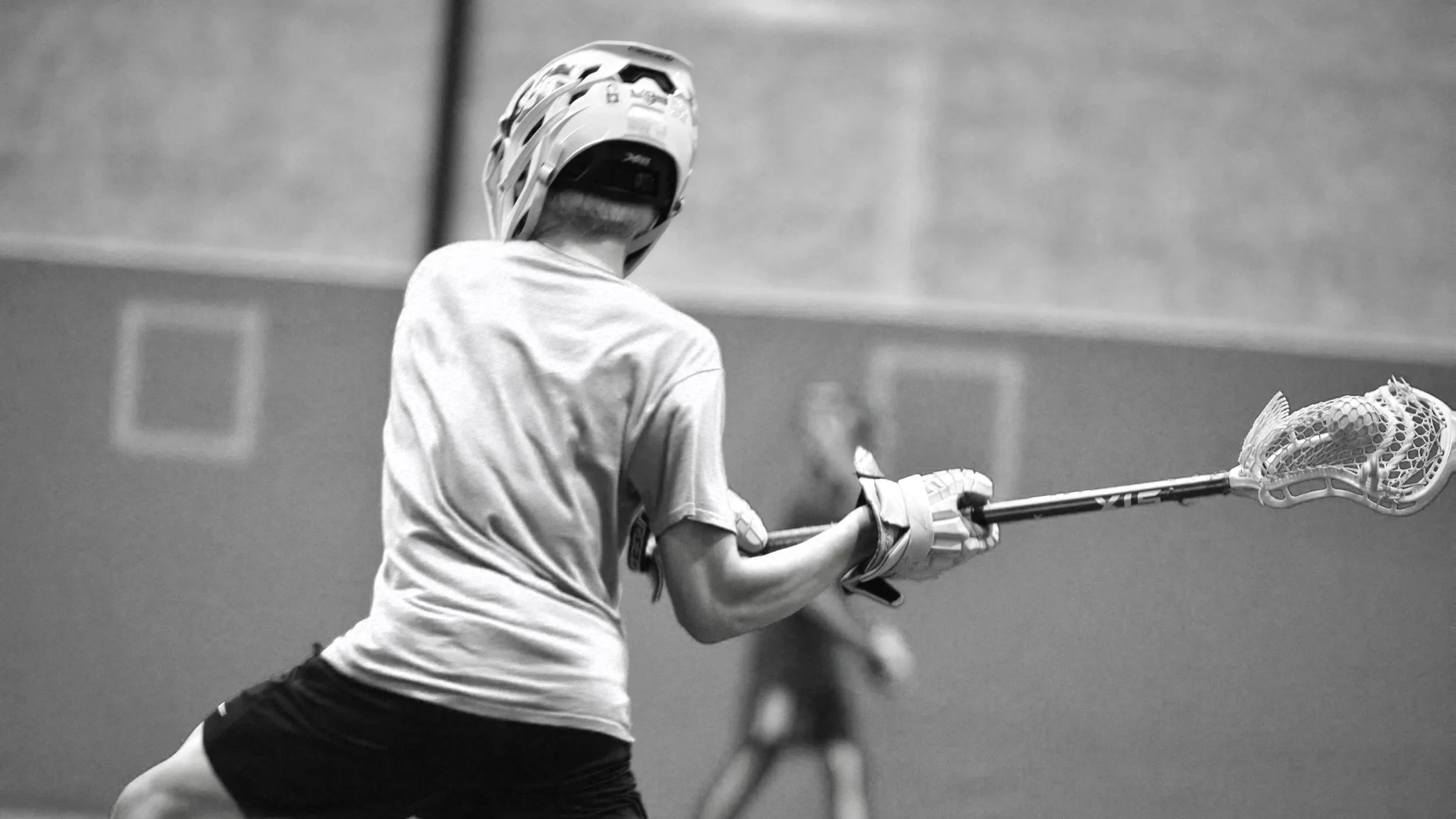 A person wearing a helmet and sports attire holding a lacrosse stick on an indoor field.