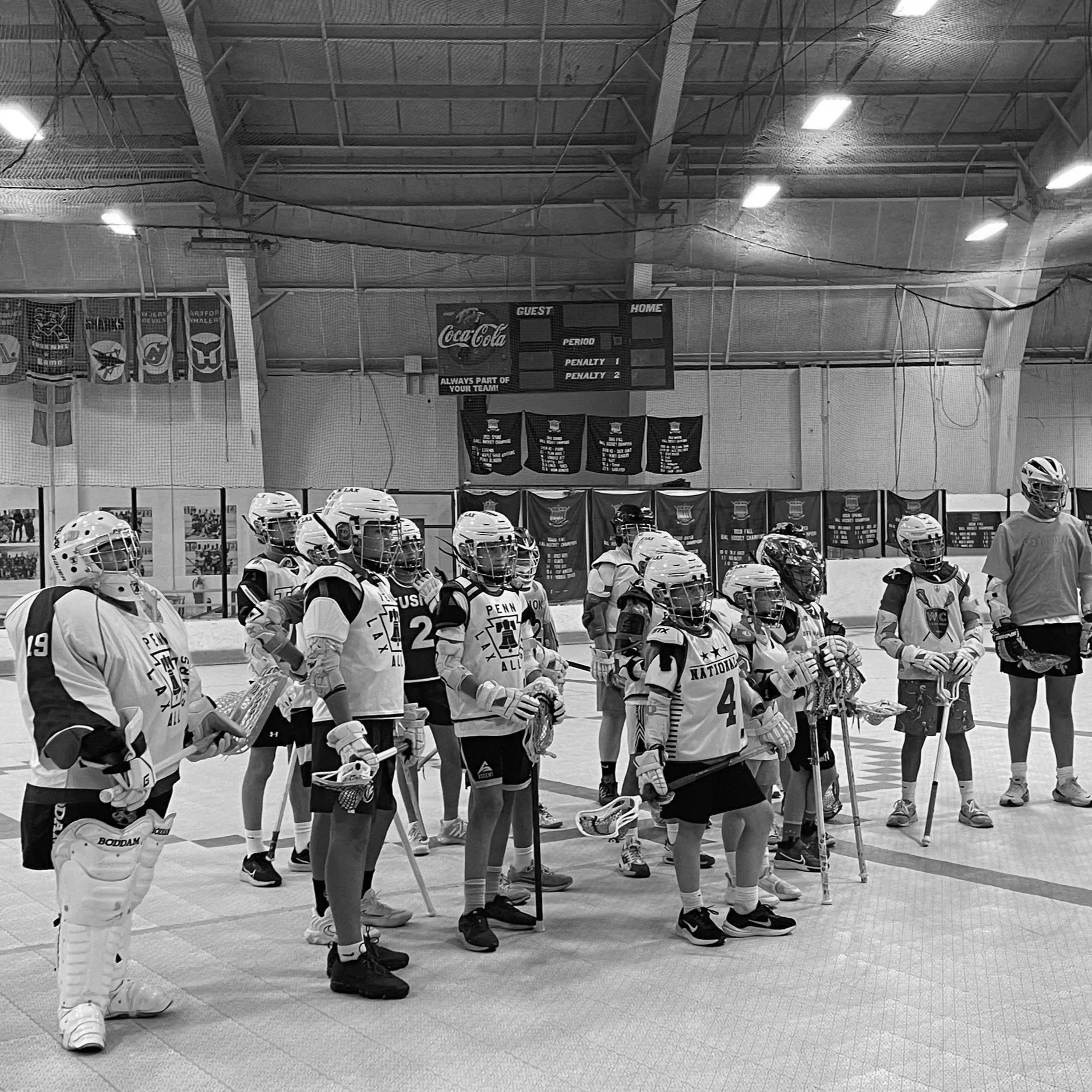 Ice hockey players in uniform standing in a line inside an indoor rink, facing a coach or instructor during a team practice or orientation.