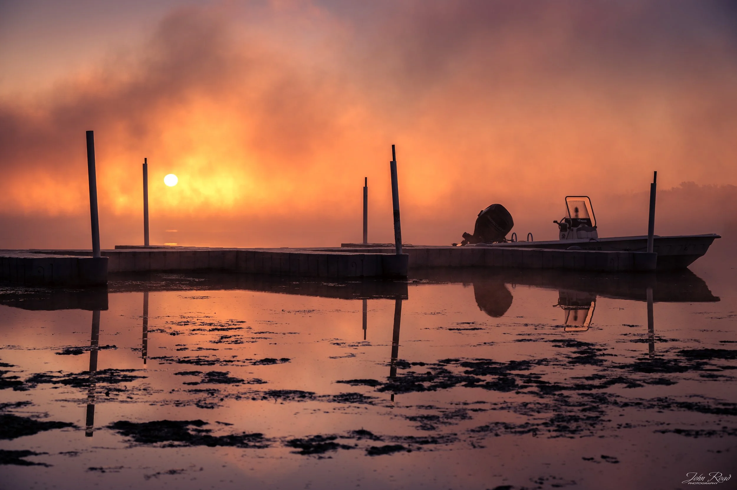 Fine art photograph of a fiery sunrise reflected over calm water, captured by John Road.