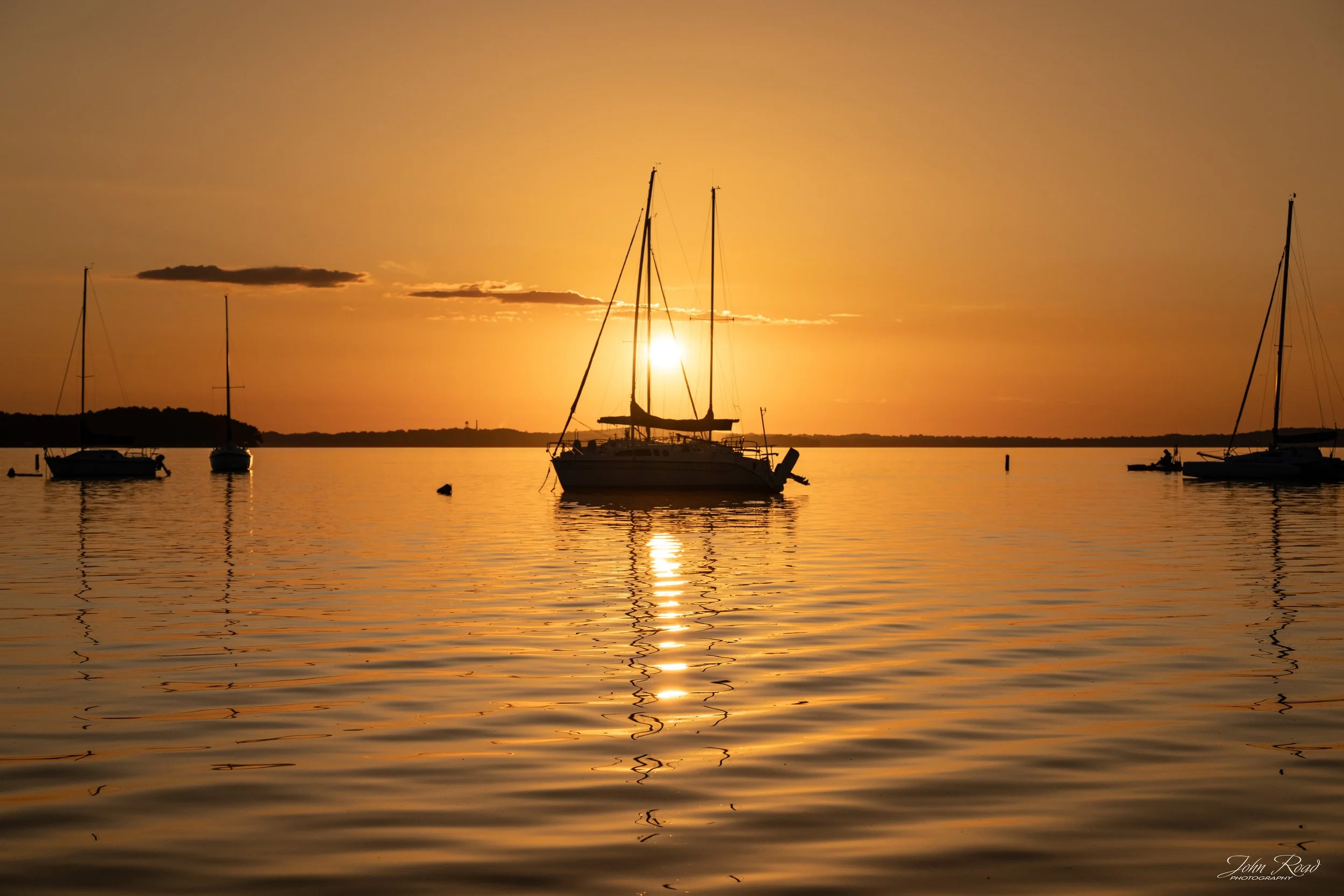 Golden Anchorage captures a quiet morning on the water as sailboats rest at anchor beneath the first light of day. Warm golden tones, gentle ripples, and a peaceful horizon create a timeless scene of stillness, reflection, and anticipation.