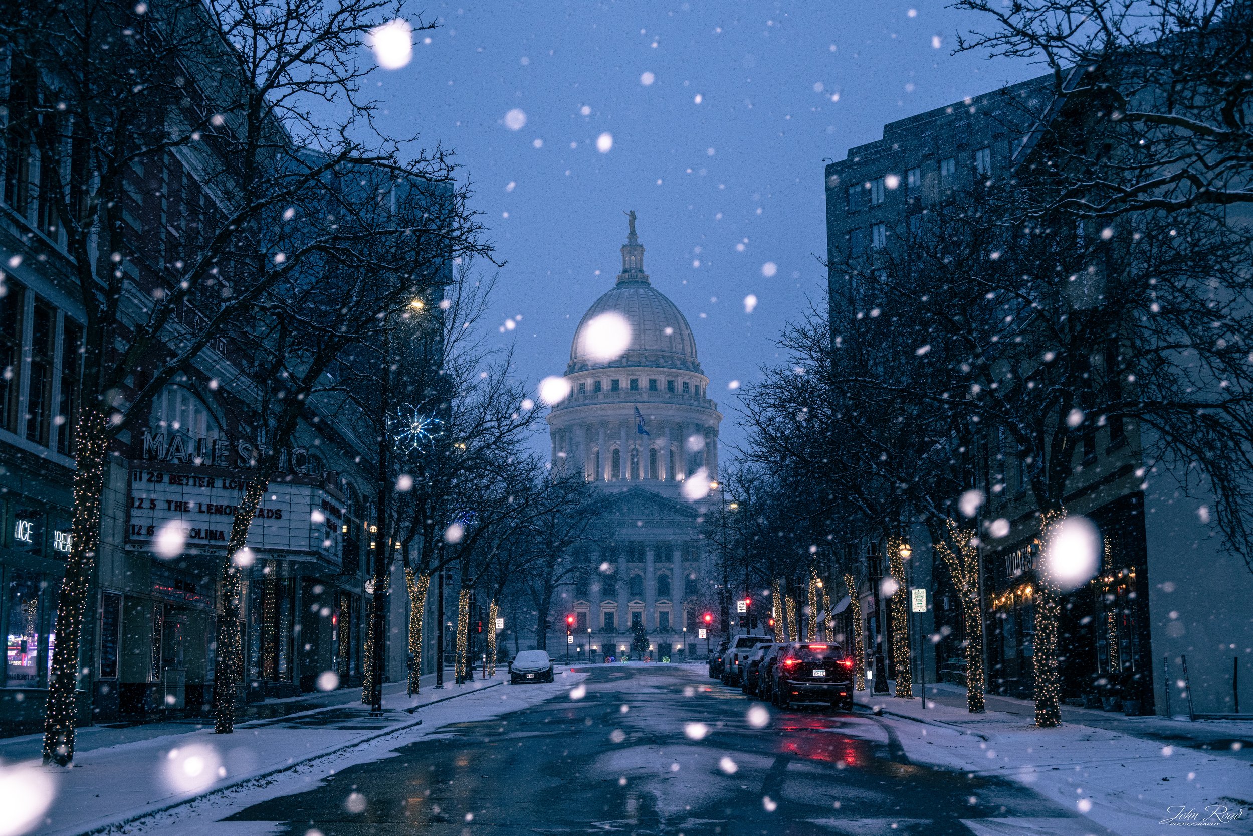 Blue hour snowfall on a quiet street leading to the Wisconsin State Capitol, photographed by John Road.