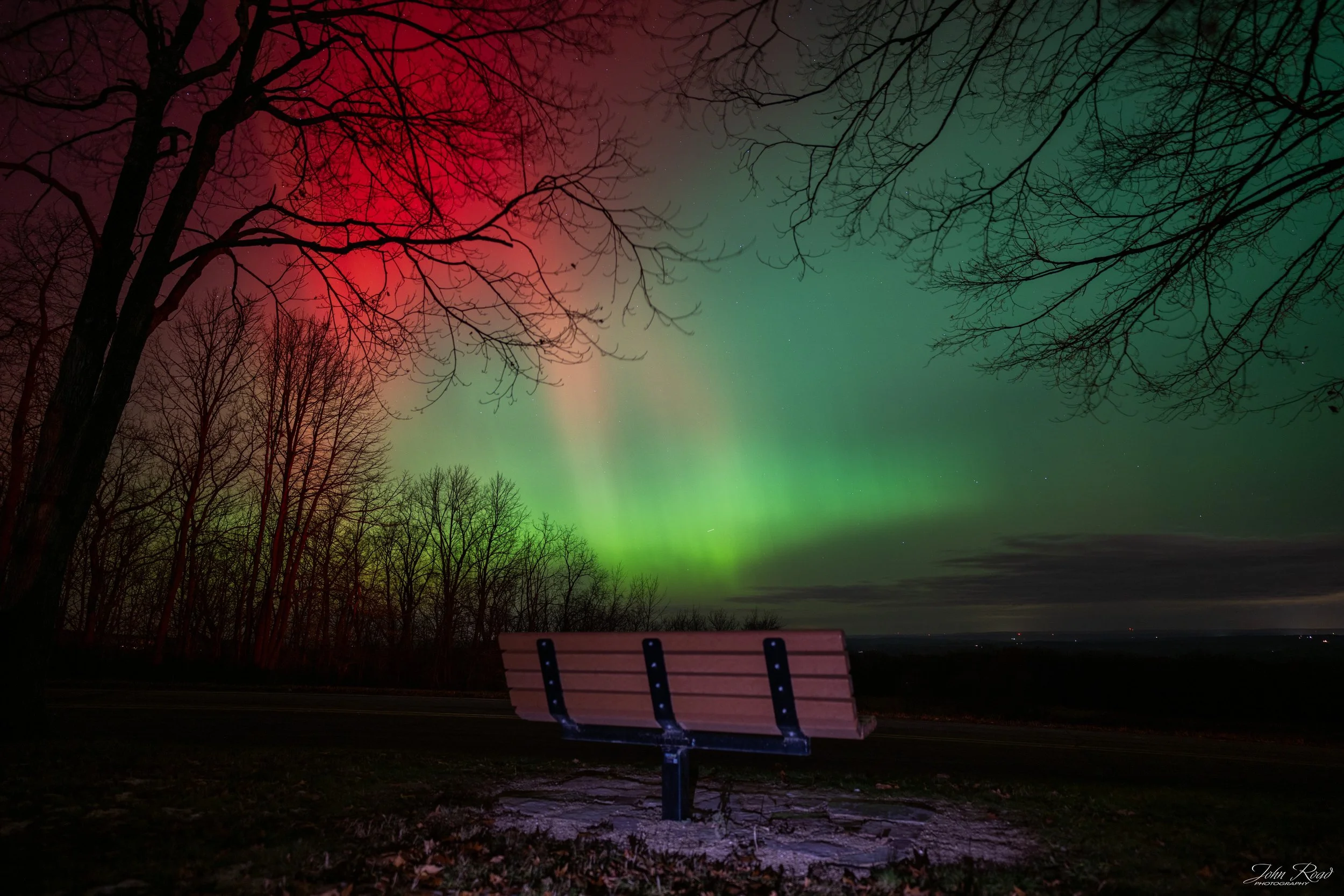 Wooden bench under red and green aurora lights in Wisconsin, fine art night photography by John Road.