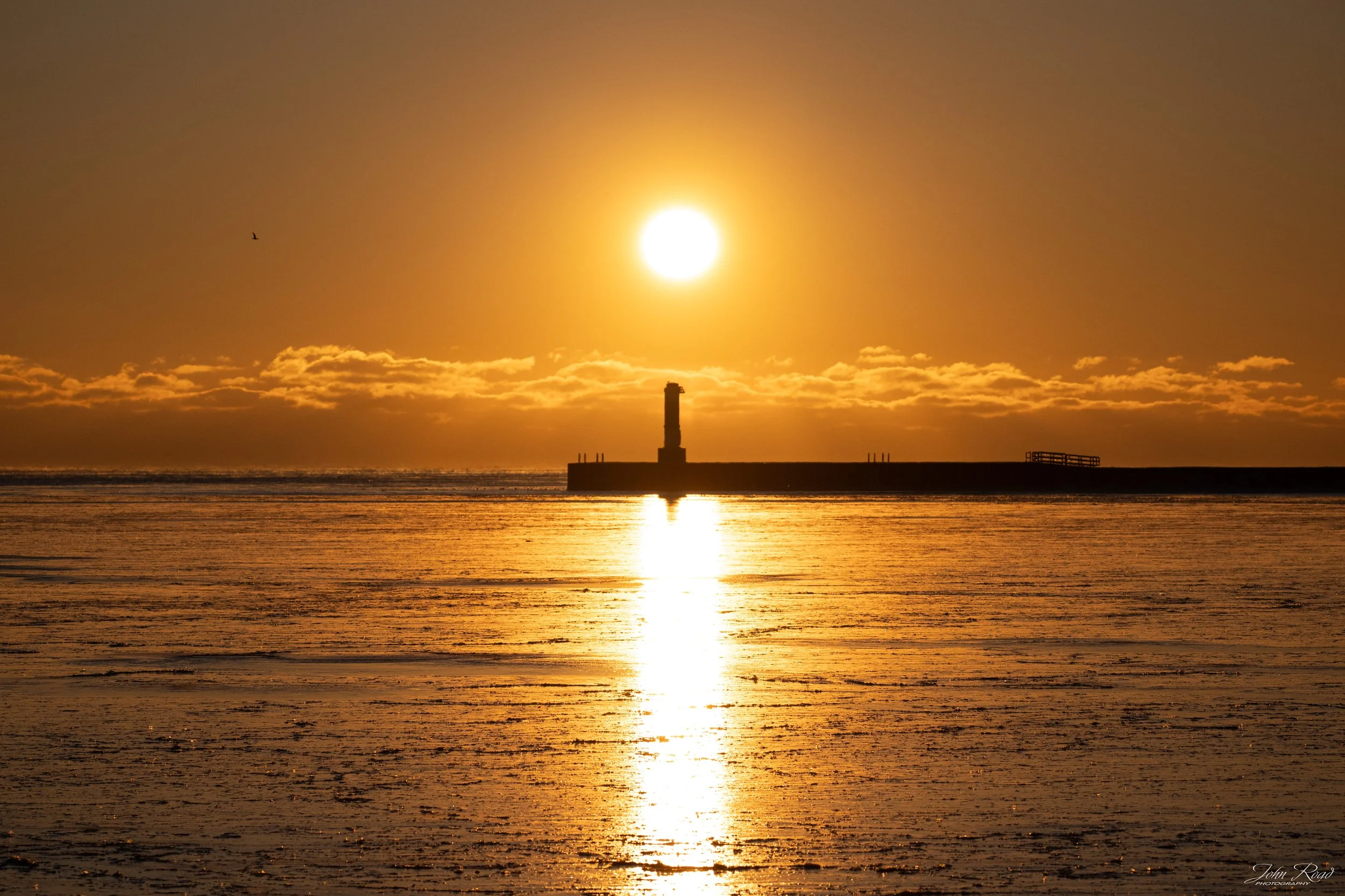 Golden winter solstice sunrise reflecting across Lake Michigan with distant lighthouse in Manitowoc, Wisconsin, fine art landscape by John Road.