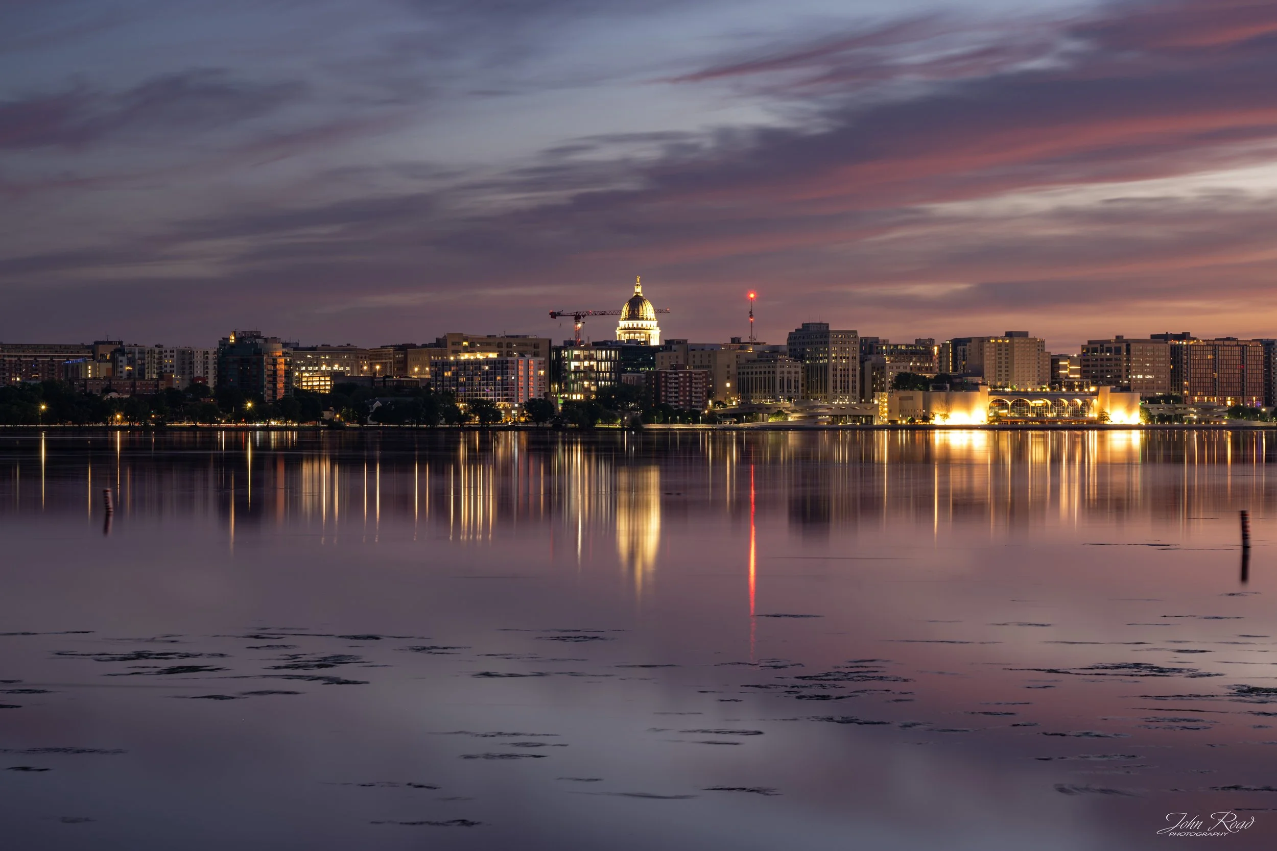 Fine art photograph of the Madison skyline and Wisconsin State Capitol reflected across Lake Monona during the transition from night to dawn. Captured in Madison, Wisconsin, this long-exposure image highlights the city’s iconic skyline, colorful morn