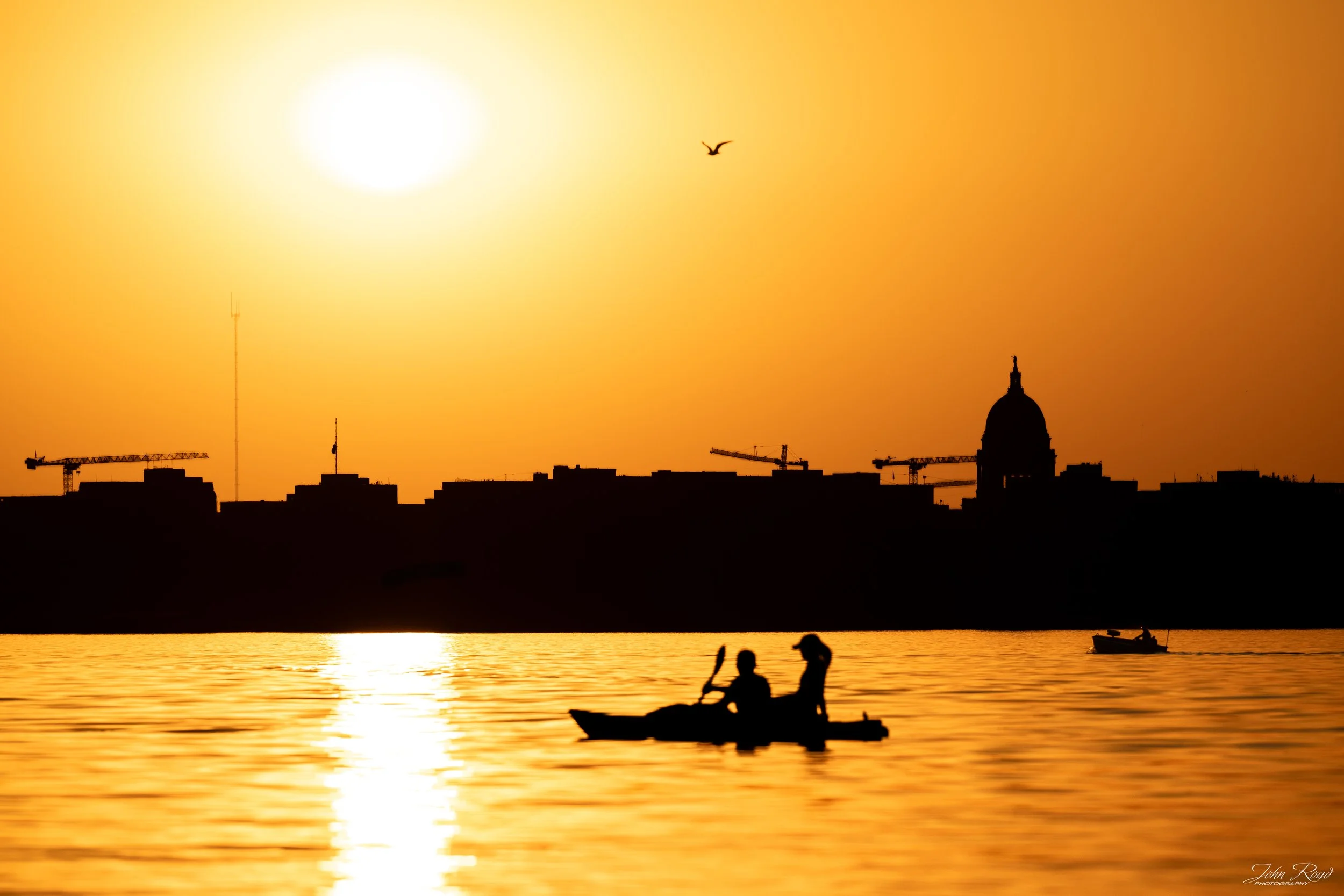 Sunset over Lake Monona with silhouettes of kayakers and Madison’s Capitol dome glowing in golden light.