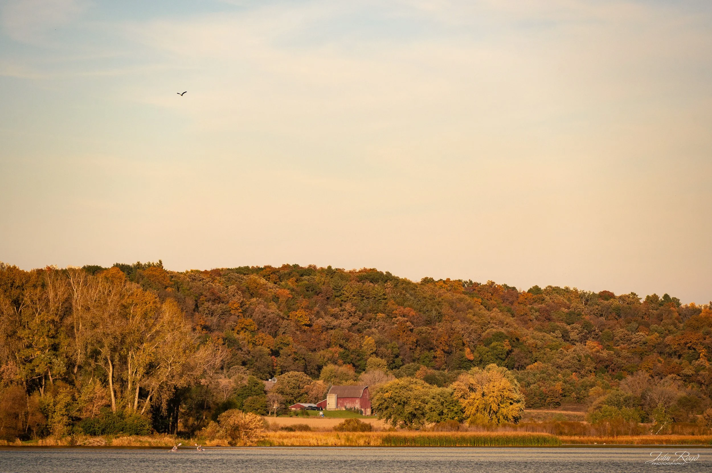 Colors of the Countryside celebrates the rich colors and quiet charm of rural Wisconsin in autumn. Rolling hills covered in colorful foliage, a small red barn, and a peaceful lake come together to create a landscape full of seasonal character. This f