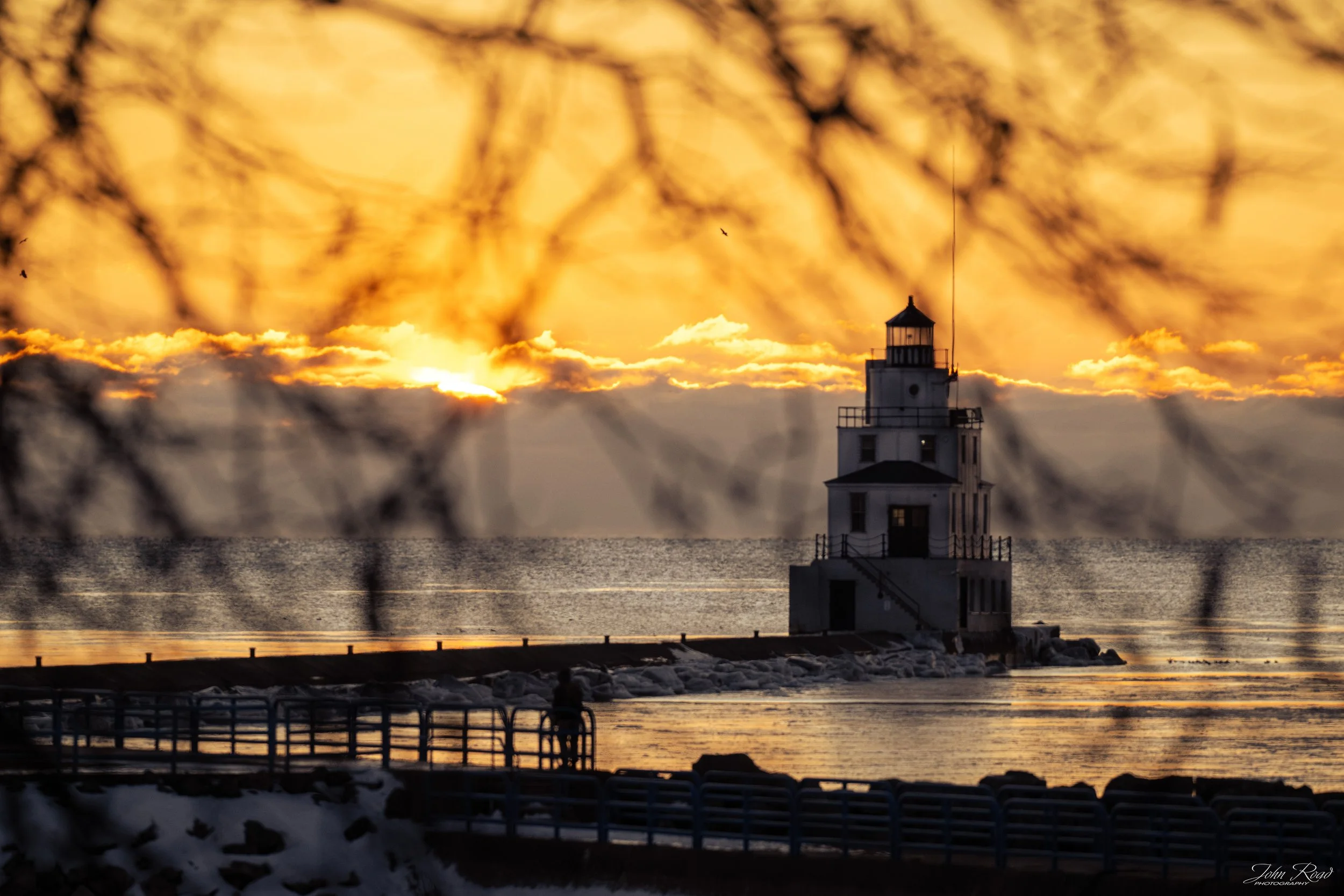 Winter solstice sunrise framed by tree branches with Manitowoc lighthouse on Lake Michigan, Wisconsin, fine art photograph by John Road.