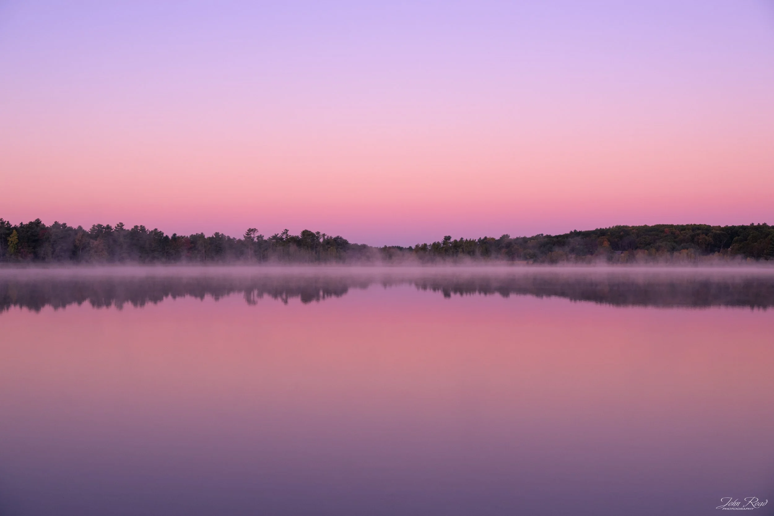 Fine art photograph of a calm lake with pink and violet reflections at sunrise, captured by John Road.