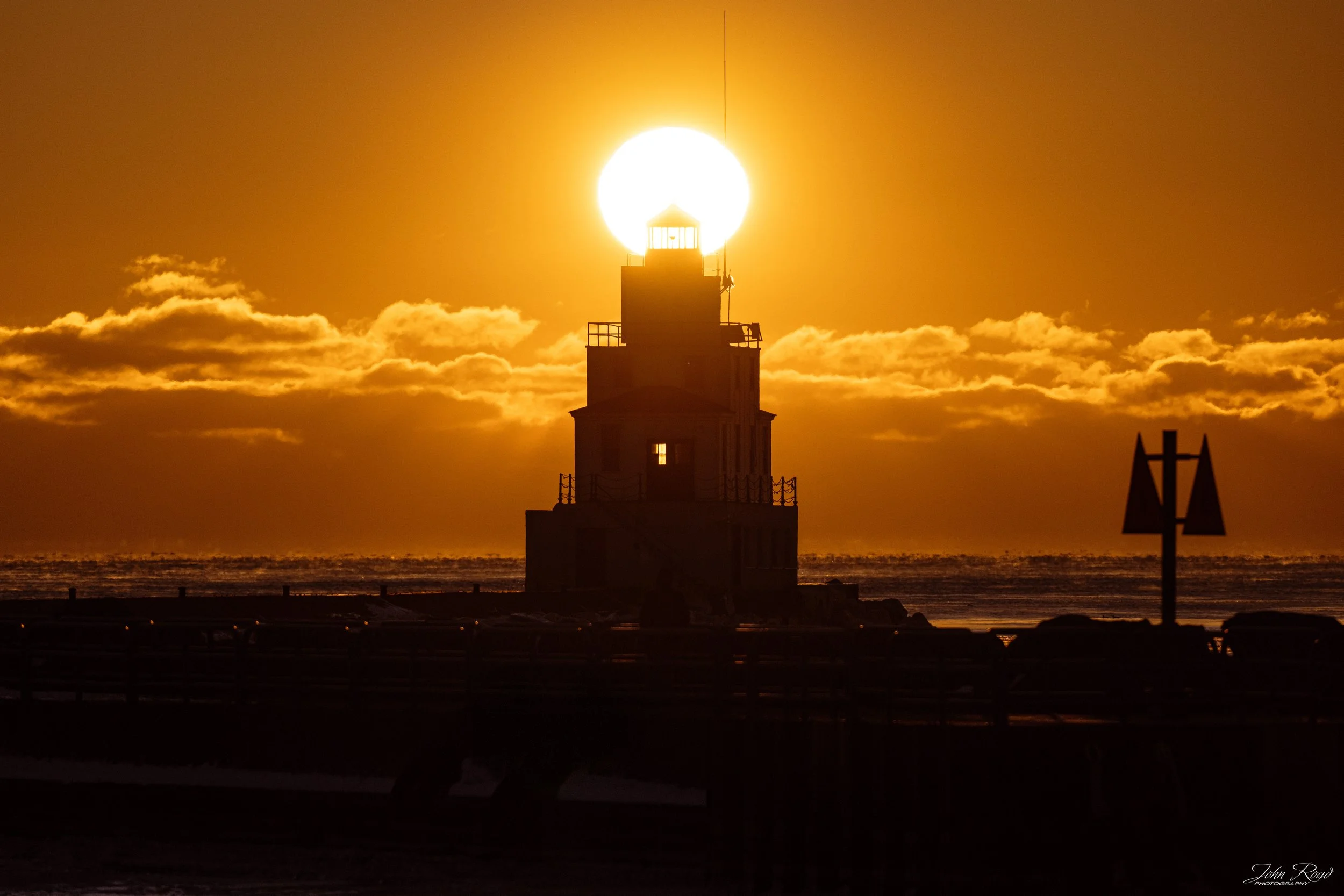 Winter solstice sunrise perfectly aligned with Manitowoc lighthouse on Lake Michigan, golden light and dramatic clouds, fine art photograph by John Road.