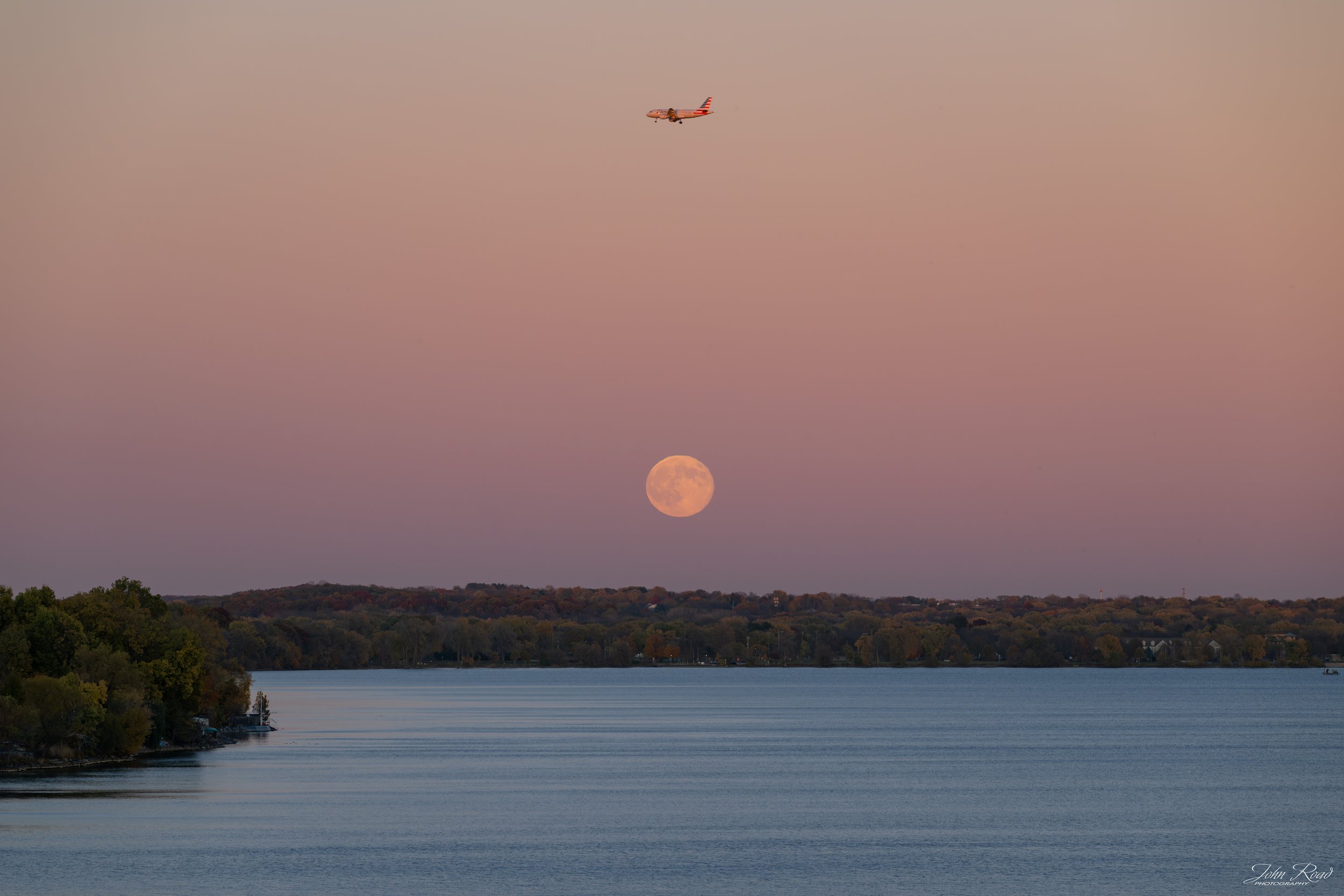 Airplane flying across the full Beaver Moon above Lake Monona in Madison, Wisconsin, photographed by John Road.