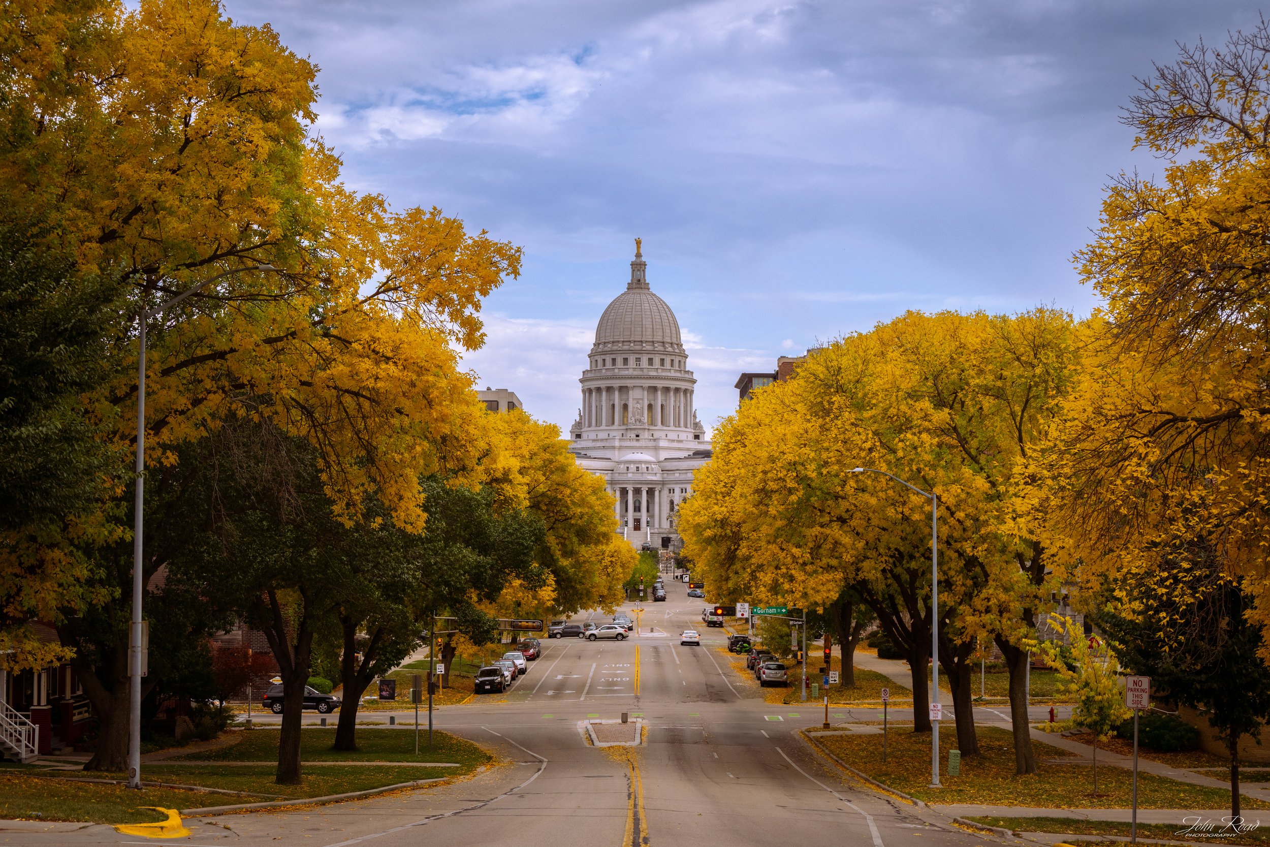Wisconsin State Capitol framed by golden fall trees on a city street in Madison, photographed by John Road.