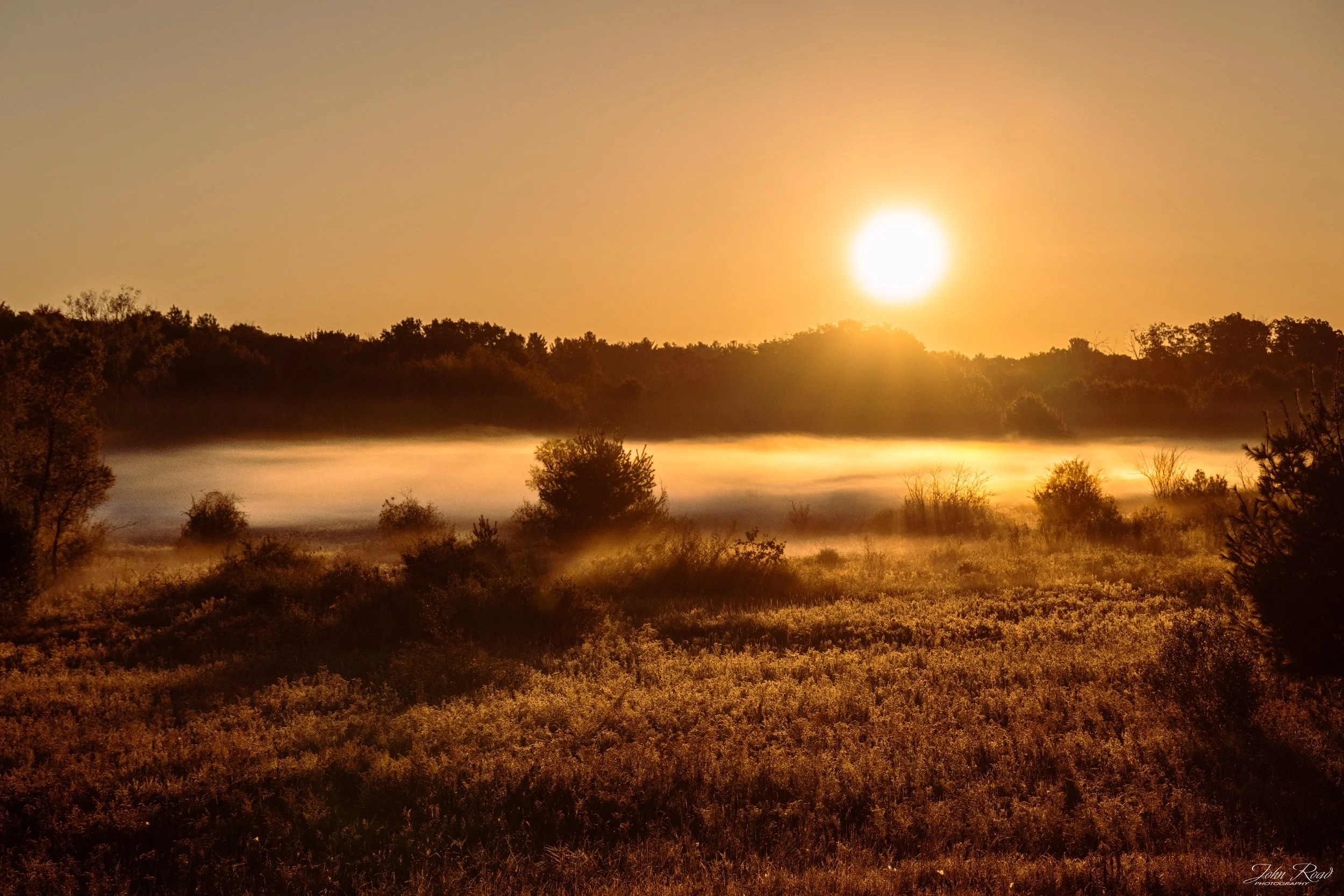 Fine art photograph of a golden sunrise over a foggy landscape, captured by John Road.