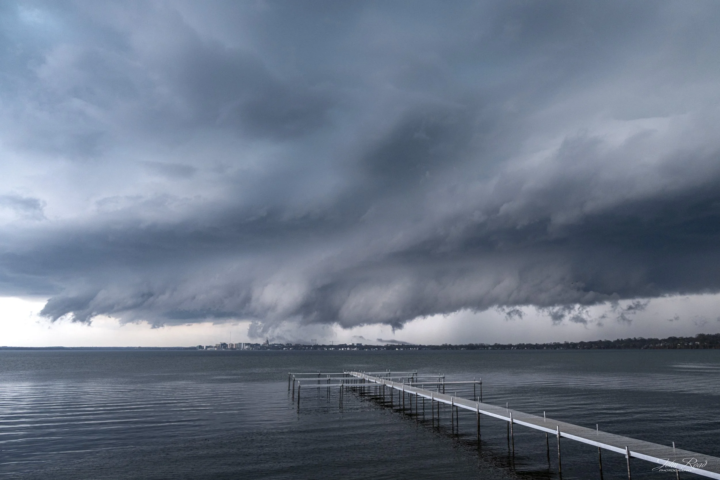 Storm clouds forming over a lake with a long pier leading into the water and distant shoreline